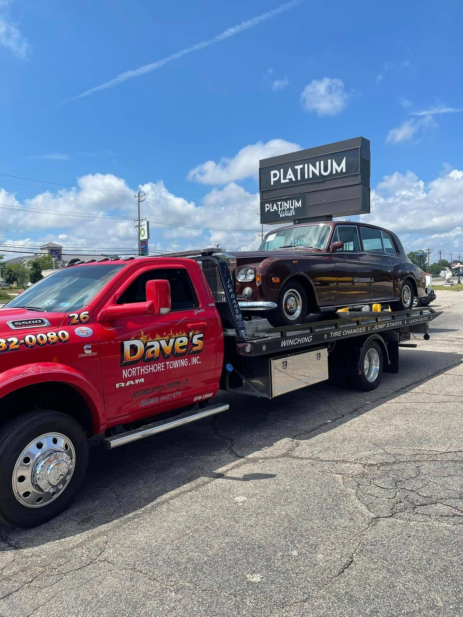 A red tow truck is towing a car in a parking lot.
