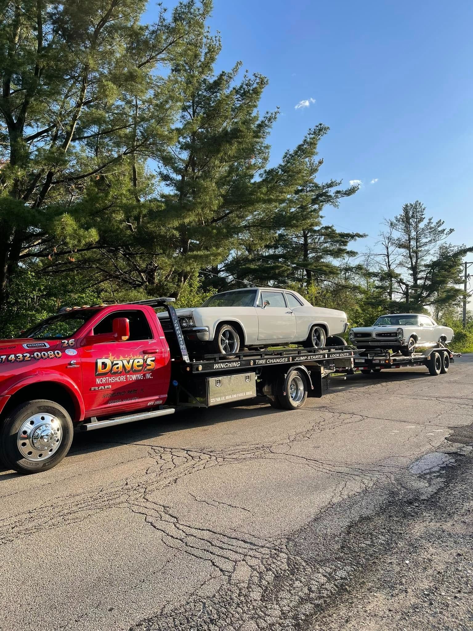 A red tow truck is carrying two cars on a trailer.