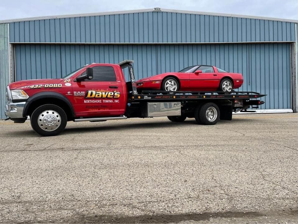 A red tow truck with a red car on the back is parked in front of a building.
