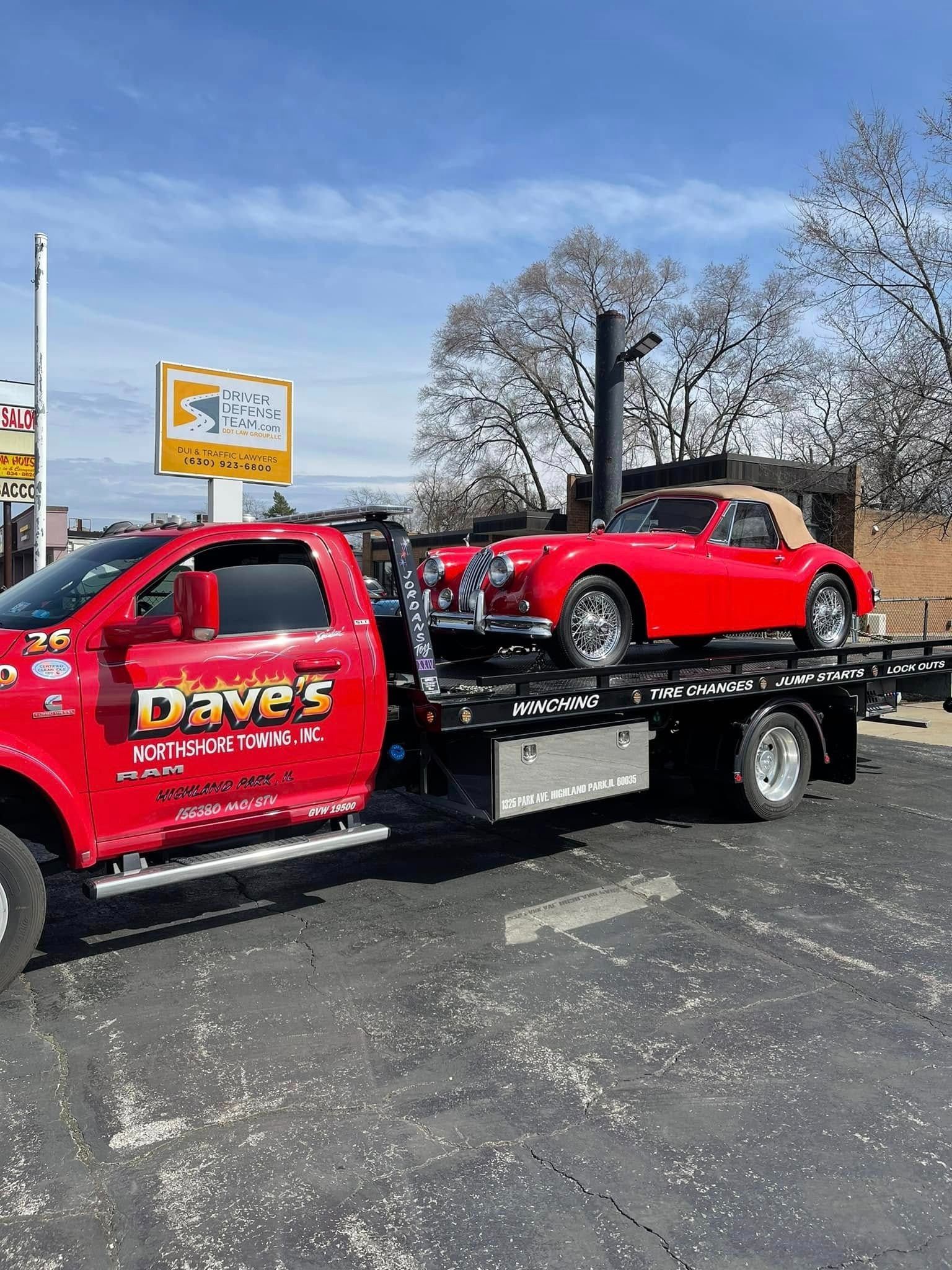 A red tow truck is towing a red sports car.