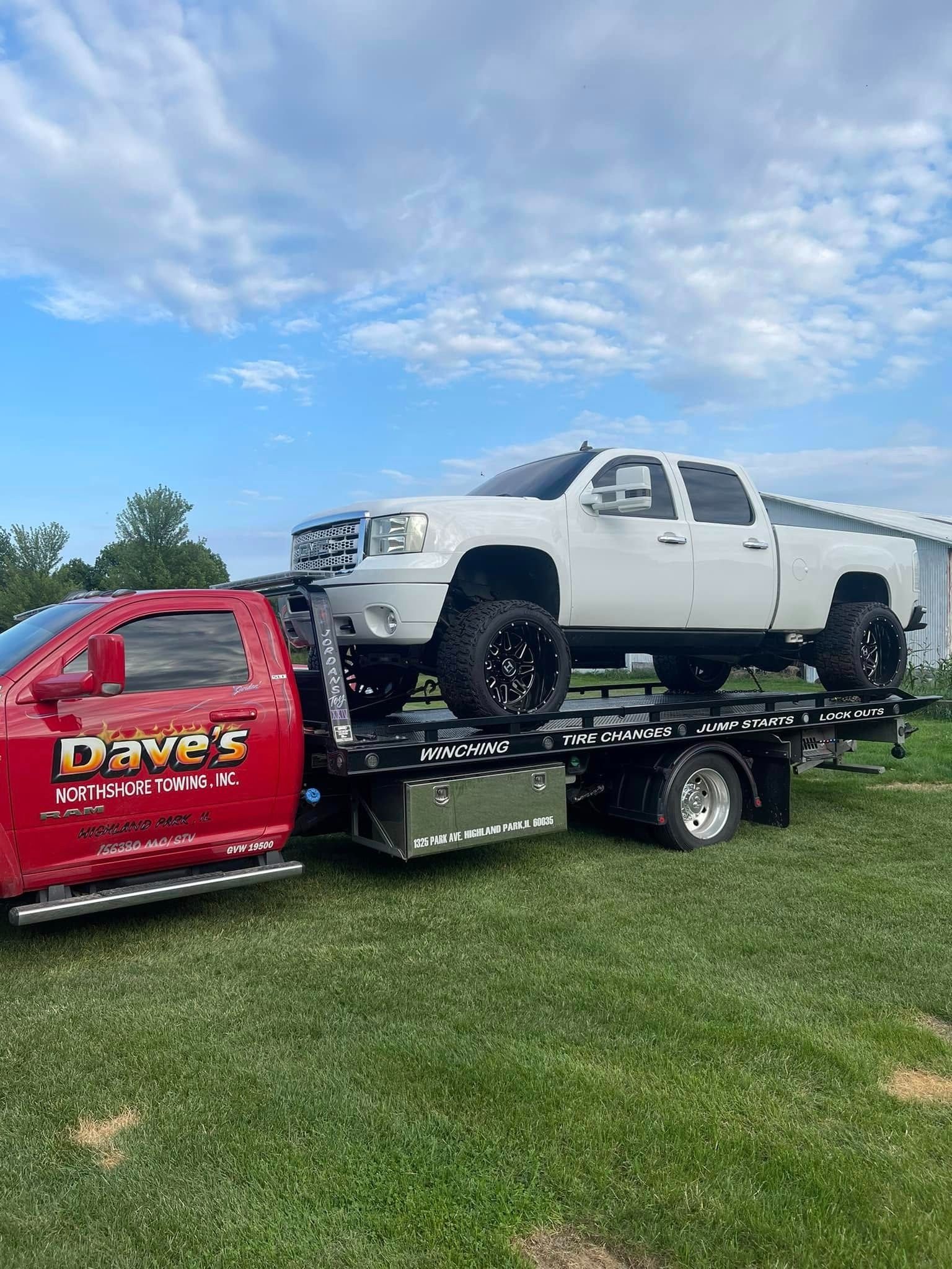 A white truck is being towed by a red tow truck.