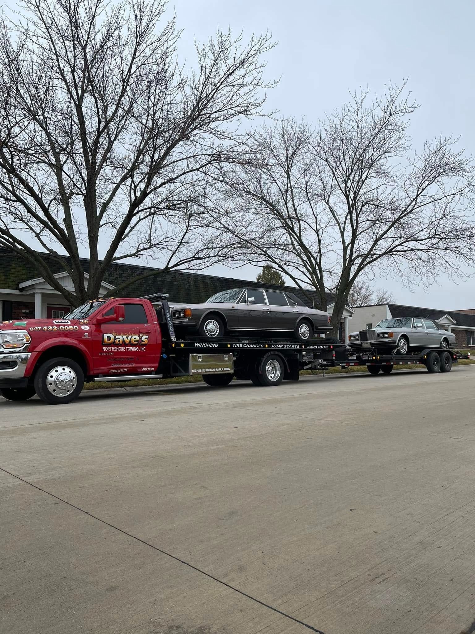 A red tow truck is towing a black car down a street.