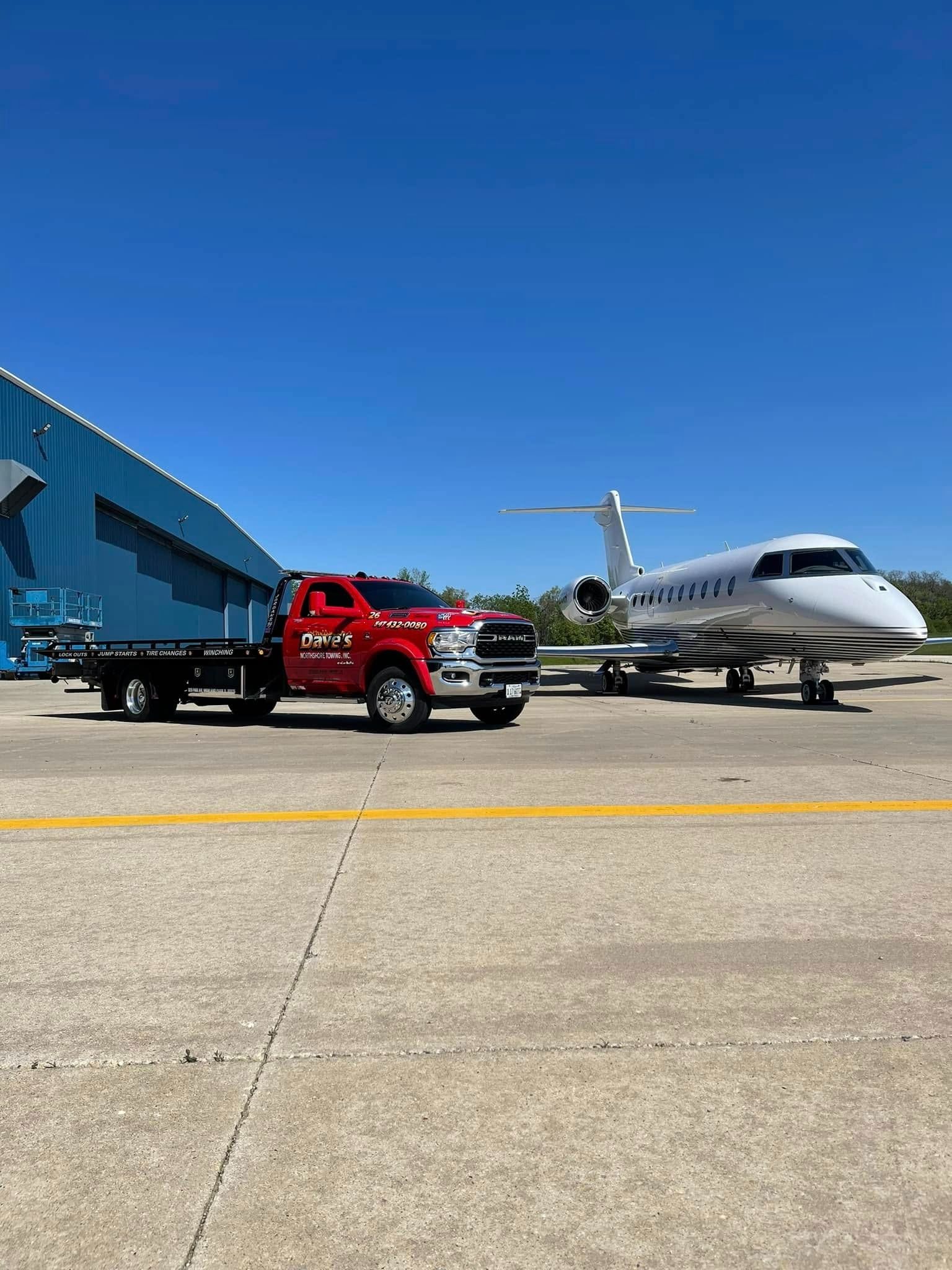 A red tow truck is towing a private jet on a runway.