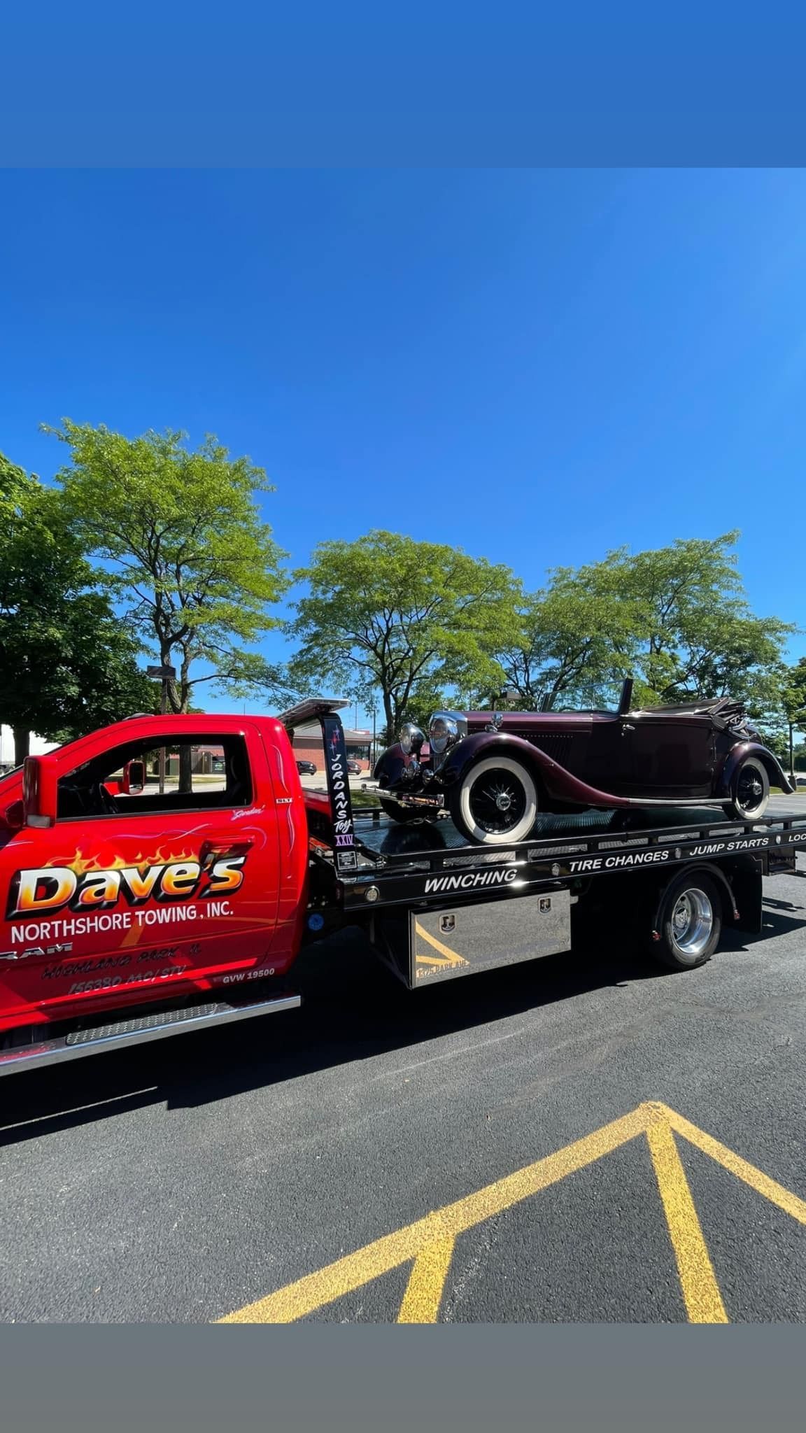 A red tow truck is towing a car on a trailer.