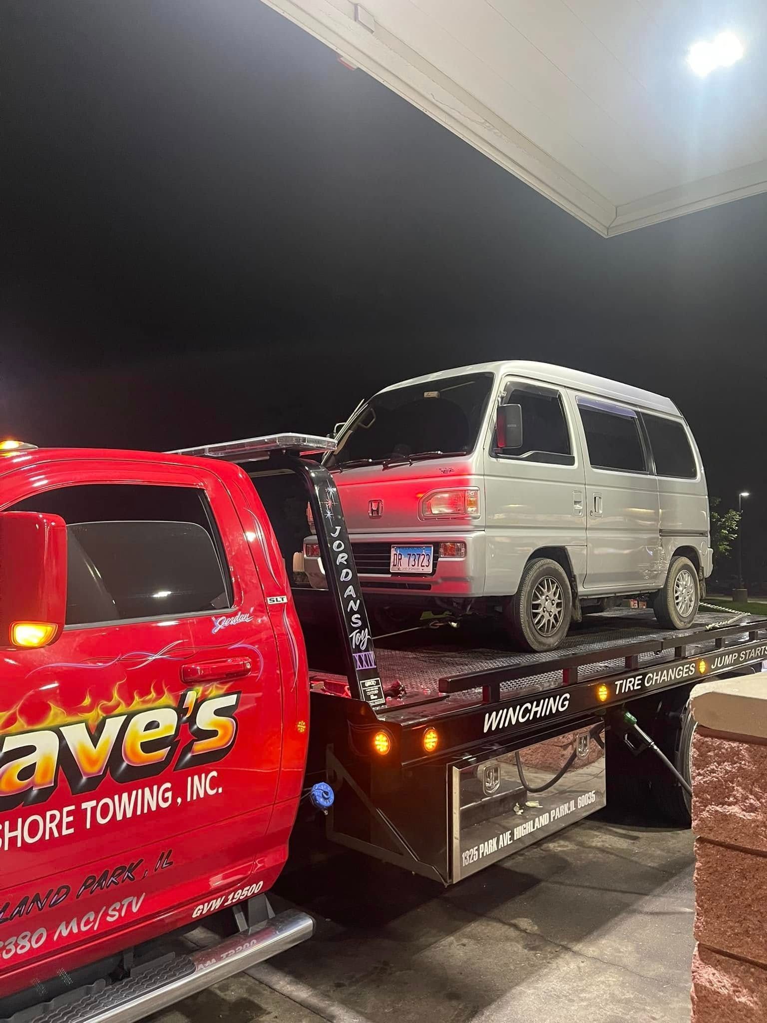 A red tow truck is towing a white van.