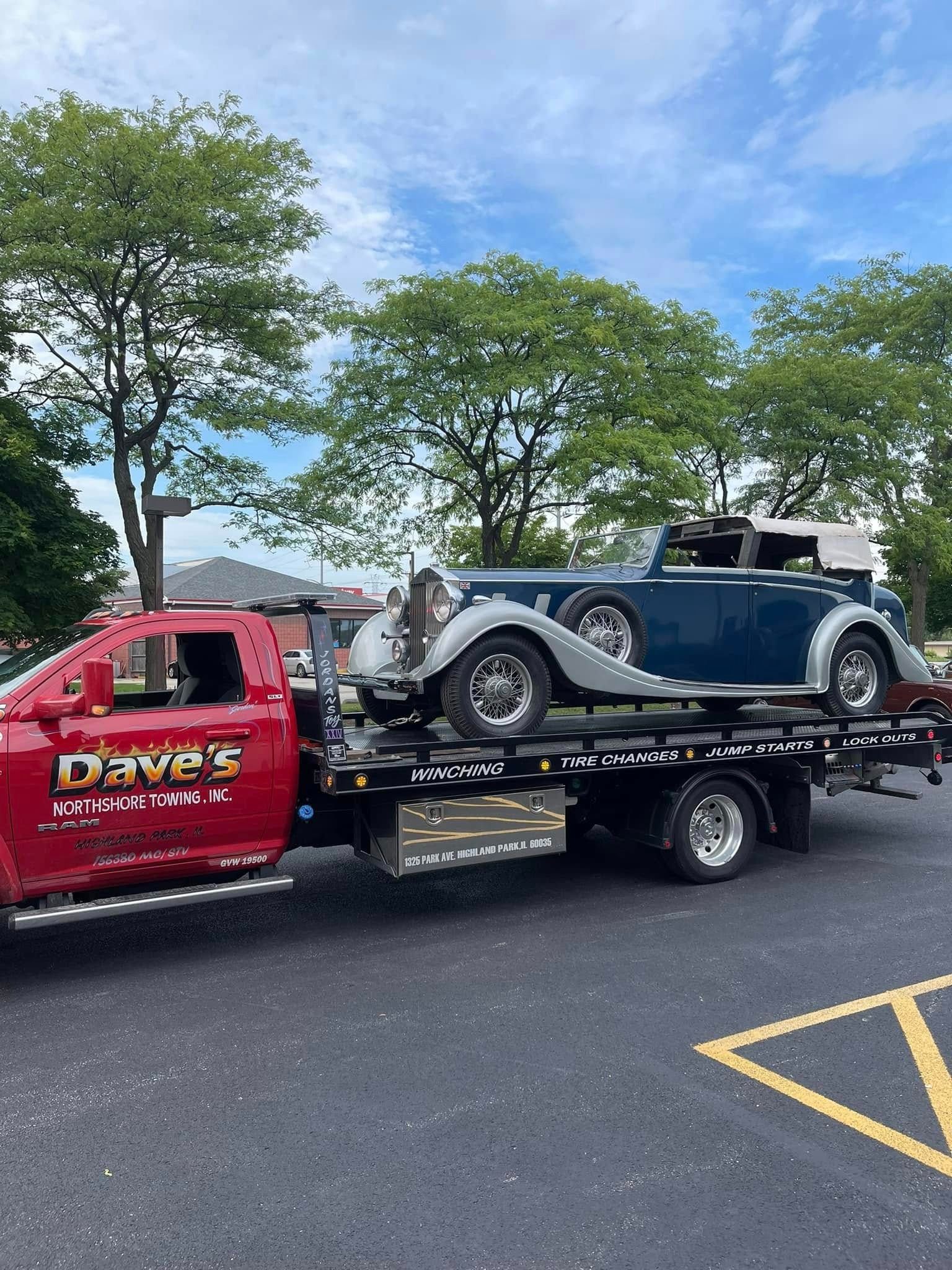 A red tow truck is towing a blue car in a parking lot.