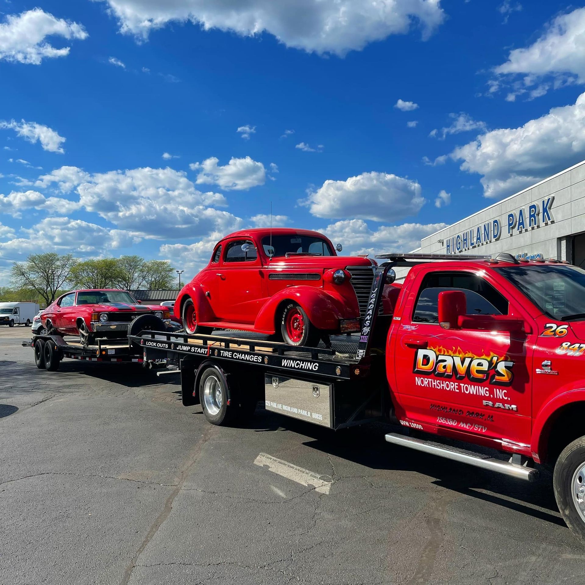 A red tow truck is towing a red car in a parking lot.