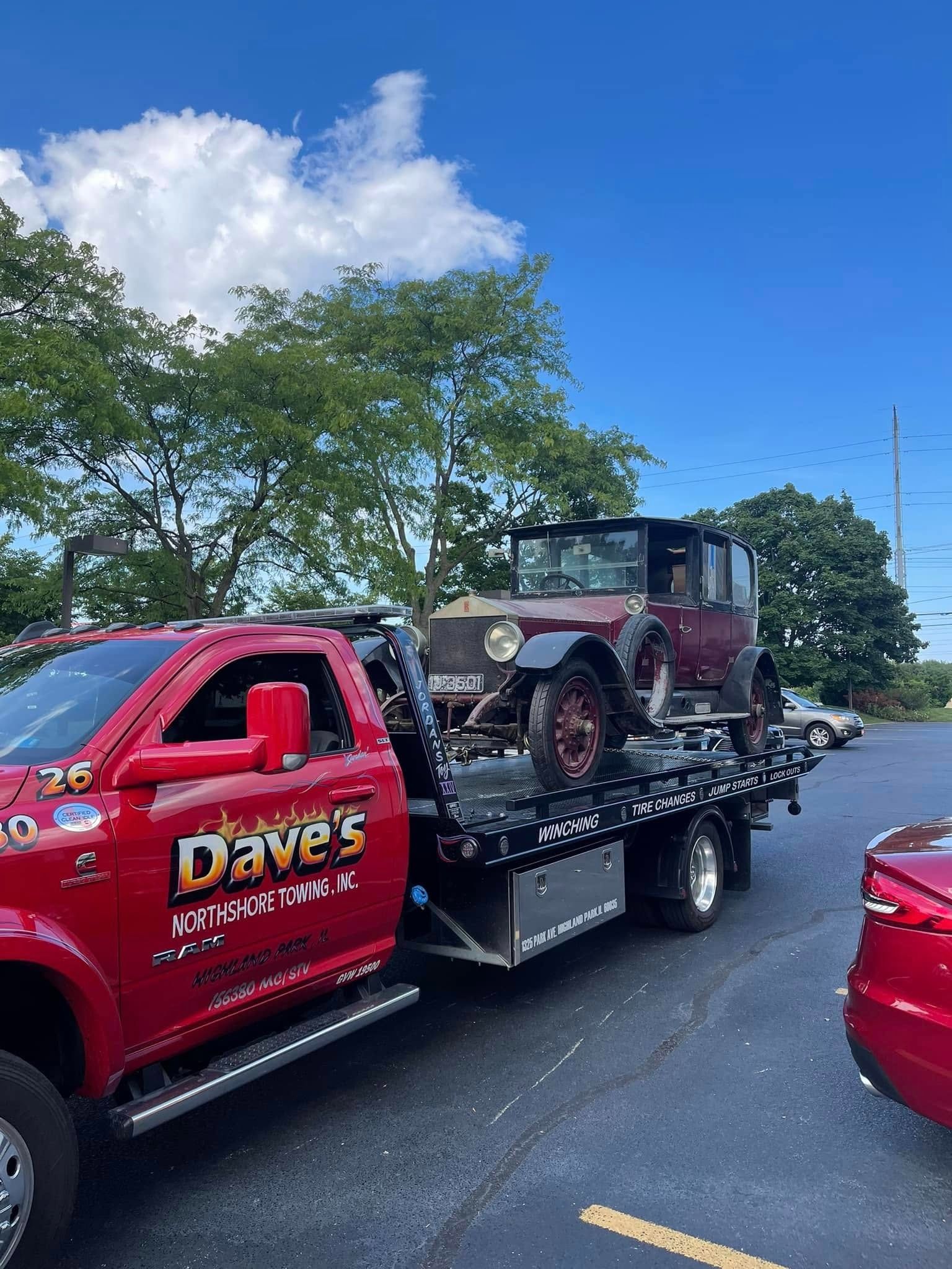 An old car is being towed by a red tow truck.