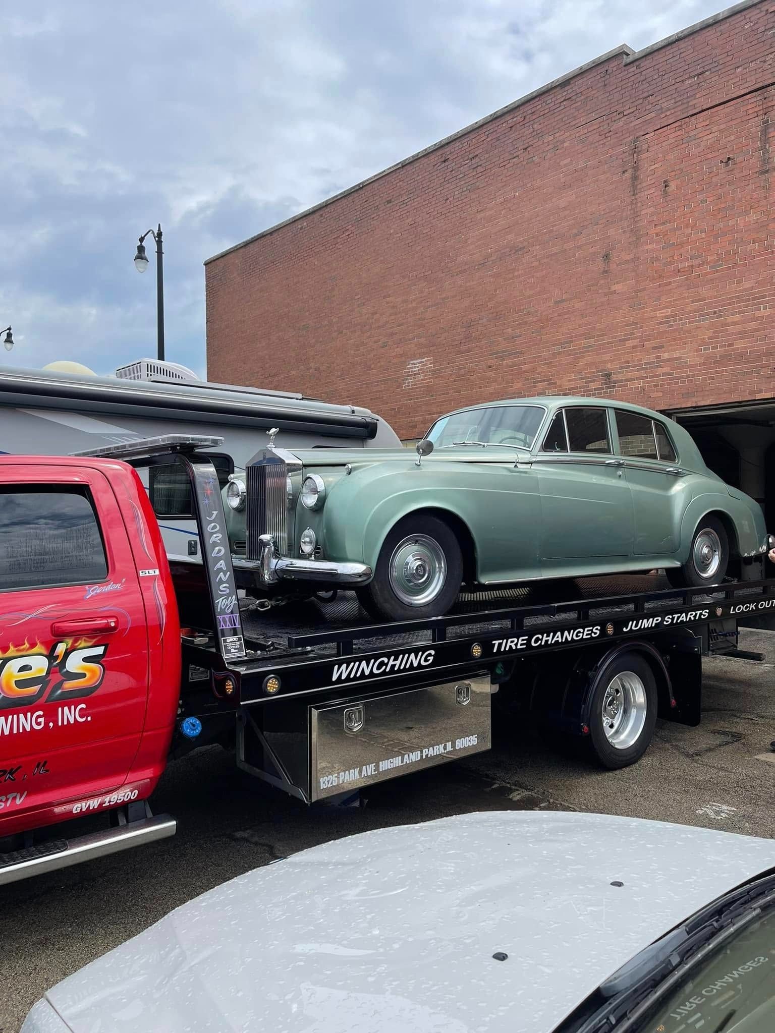 A green car is being towed by a tow truck.