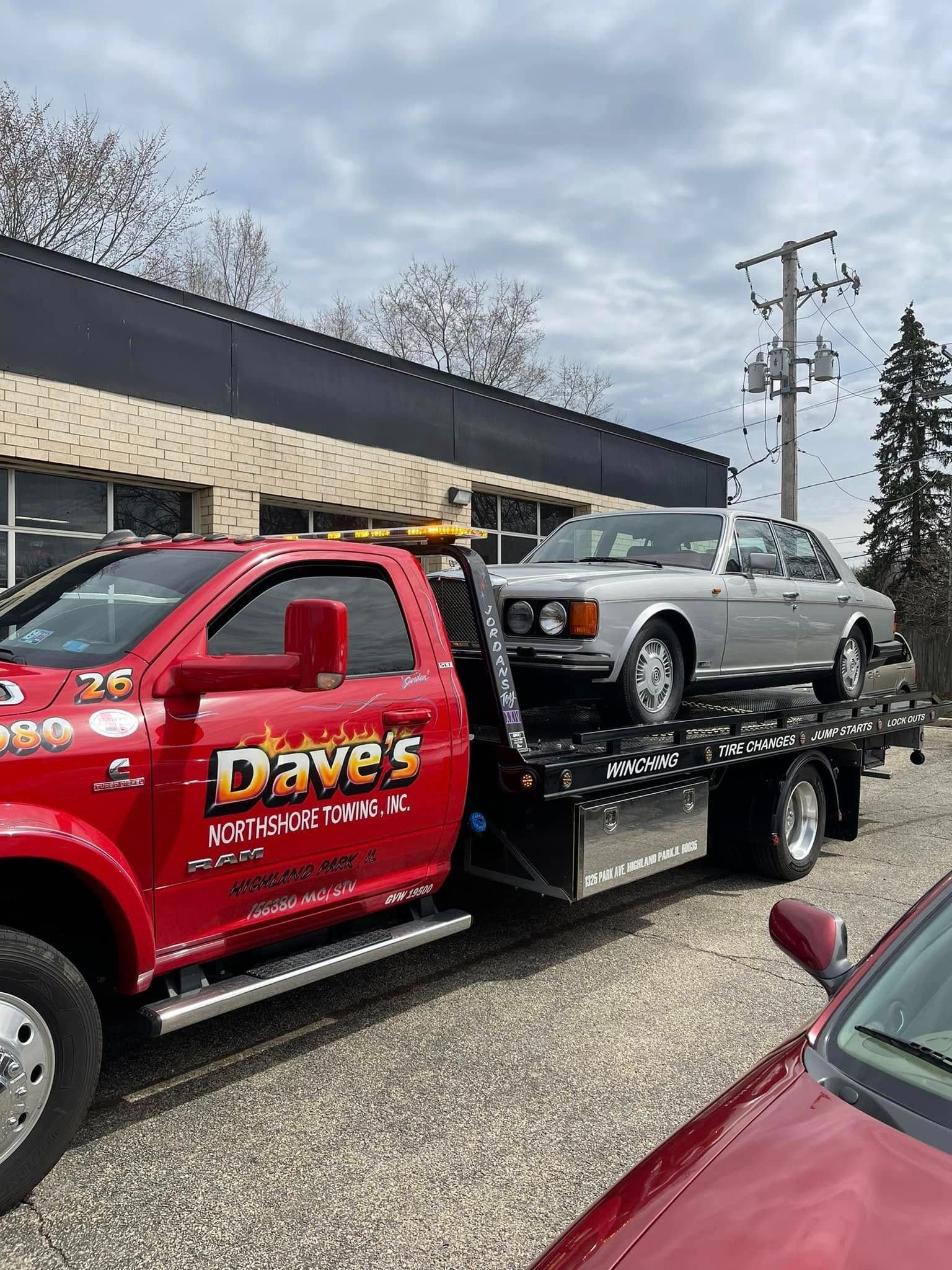A red tow truck is towing a silver car.