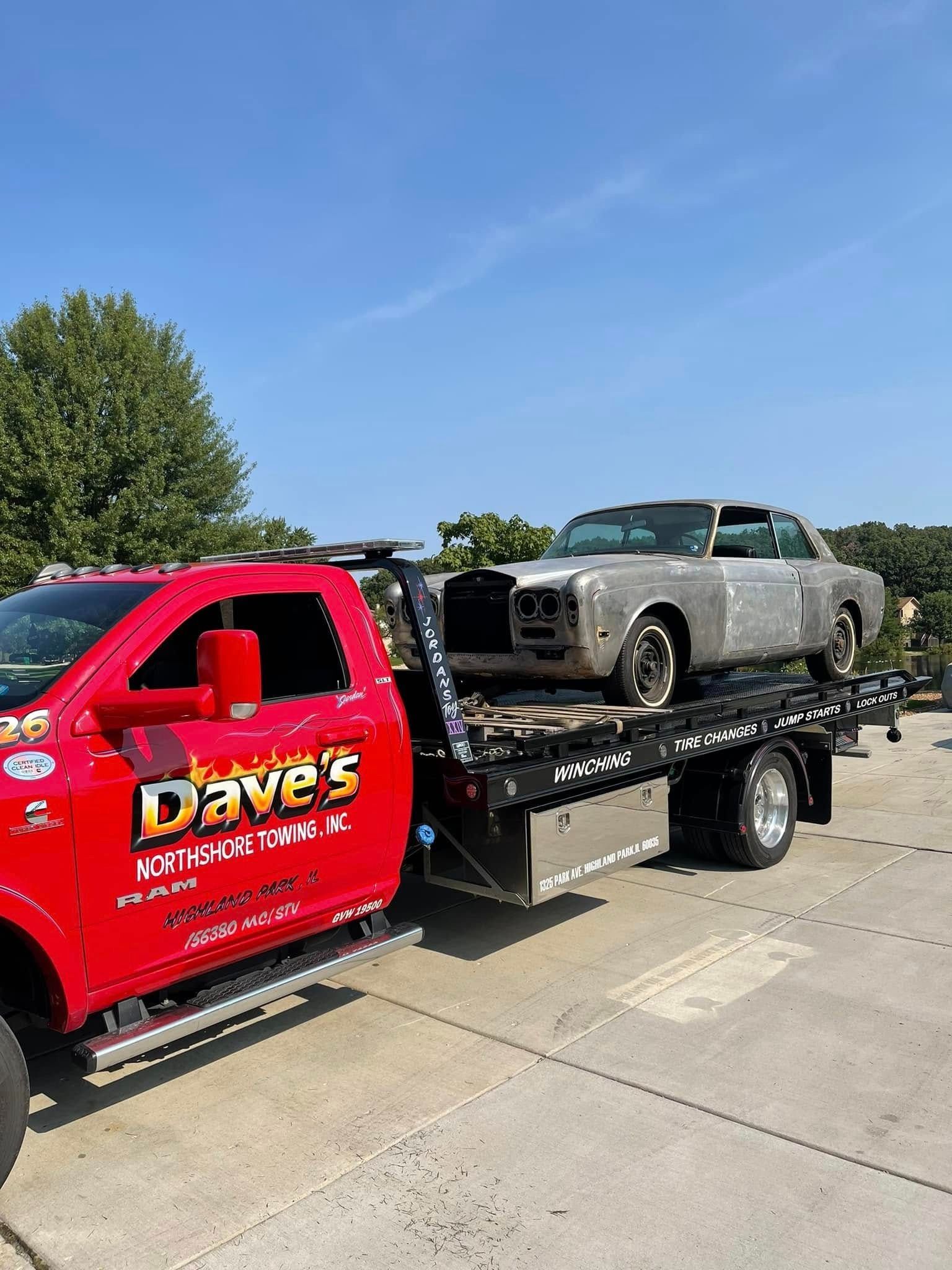 A red tow truck is towing a silver car in a parking lot.