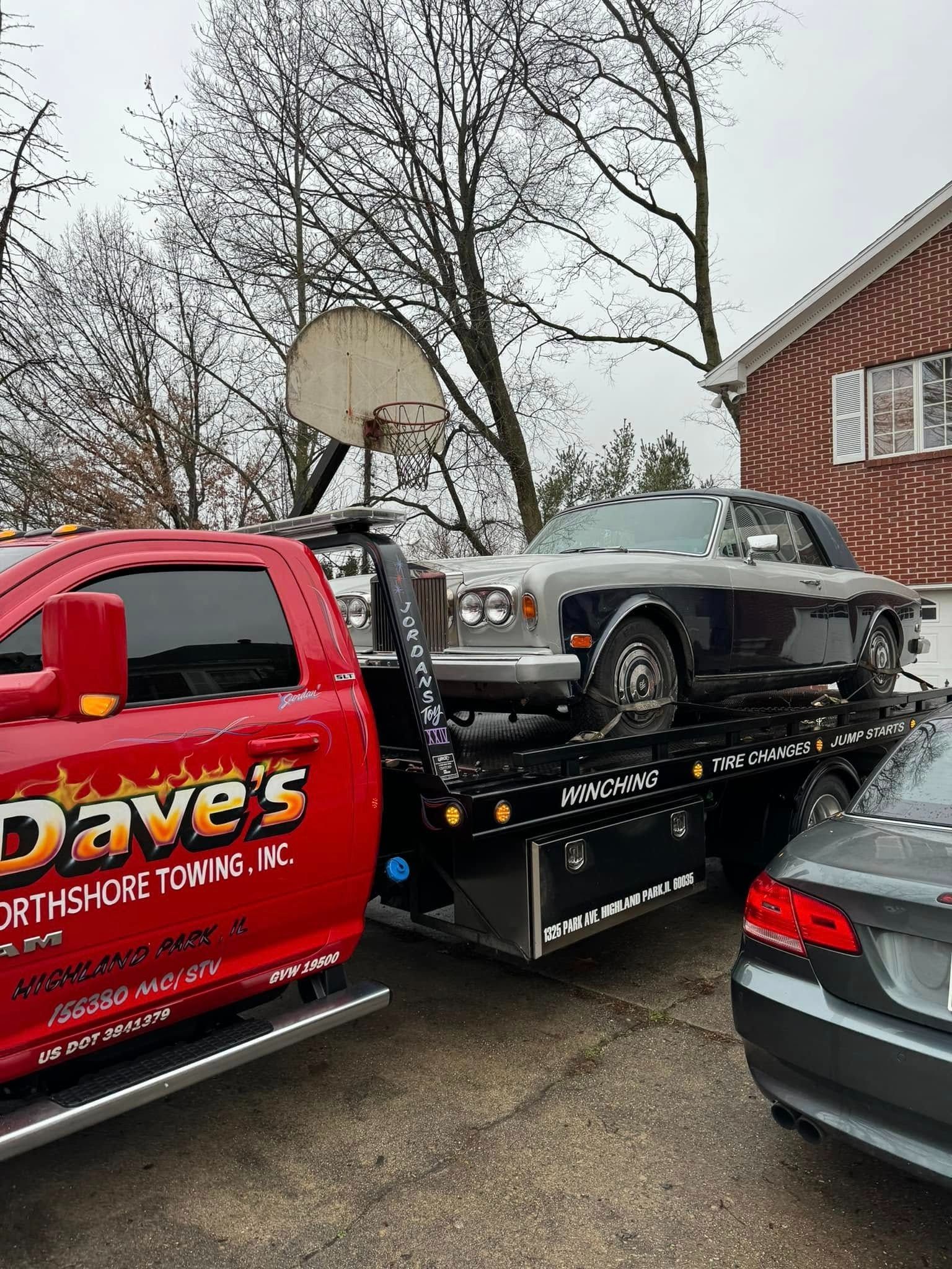 A red tow truck is carrying a car on the back of it.