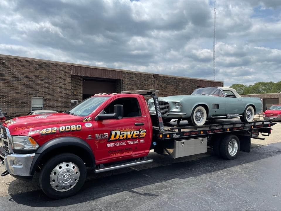 A red tow truck with two cars on the back is parked in front of a building.