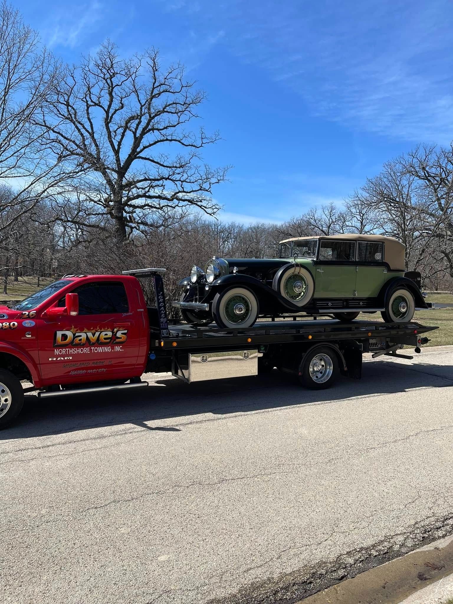 An old car is being towed by a tow truck.