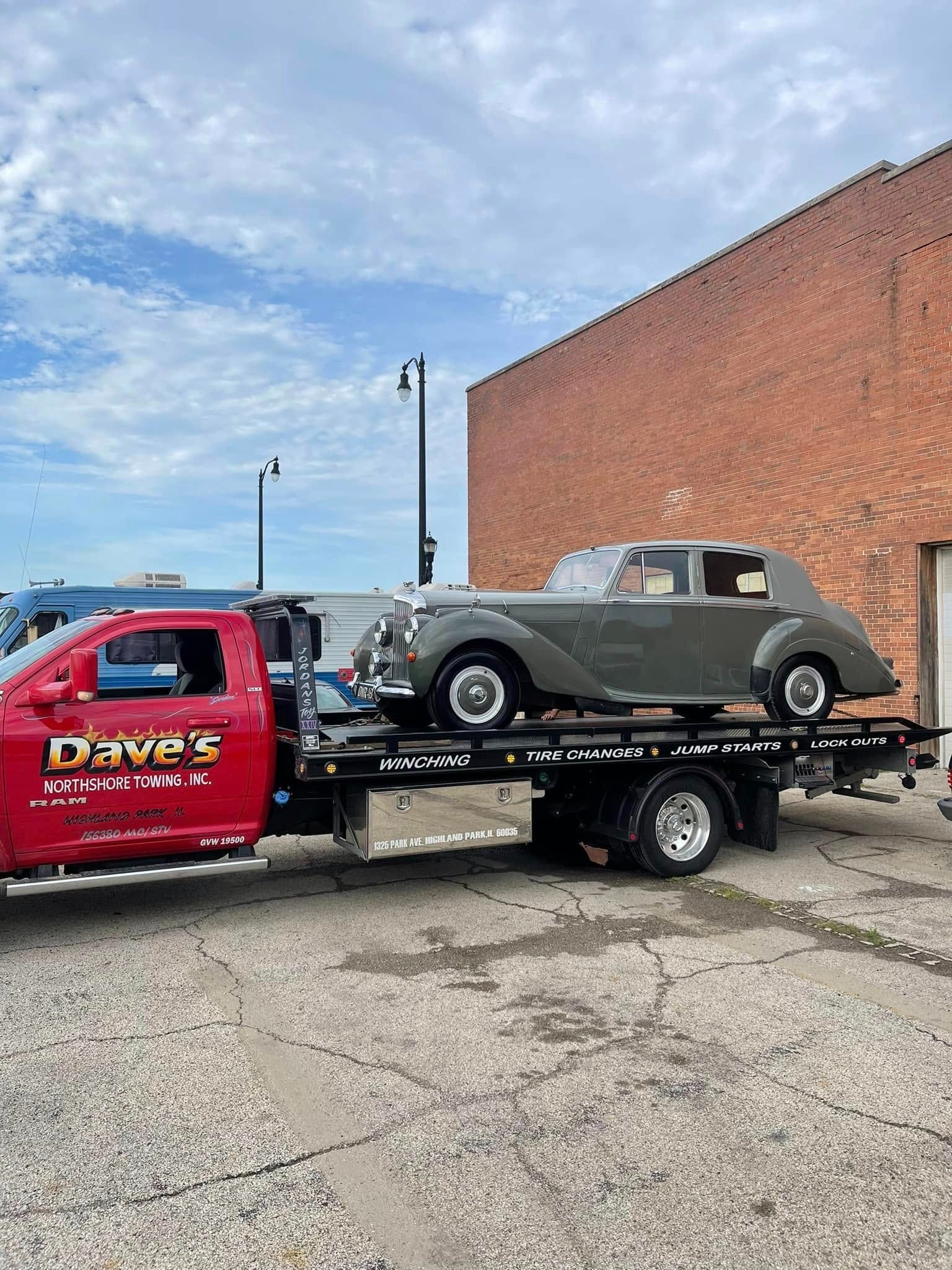 An old car is being towed by a tow truck.