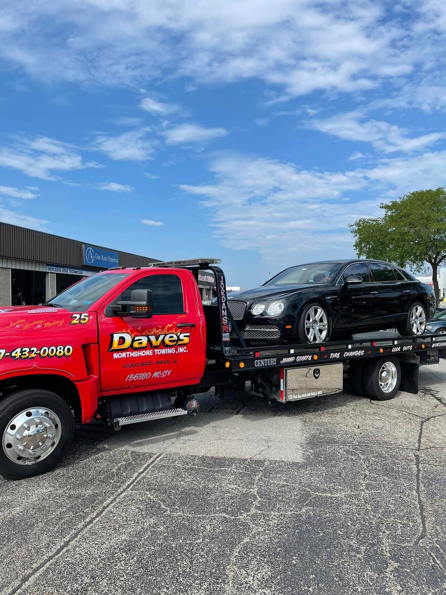 A red tow truck is towing a black car.