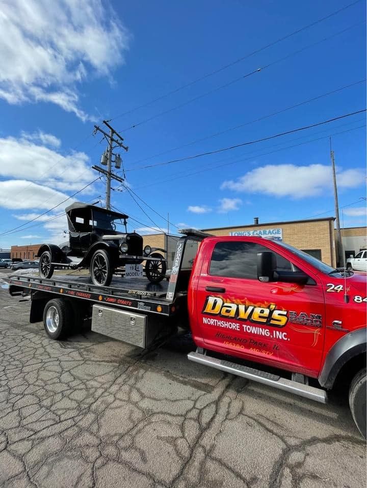 An old car is being towed by a red tow truck.