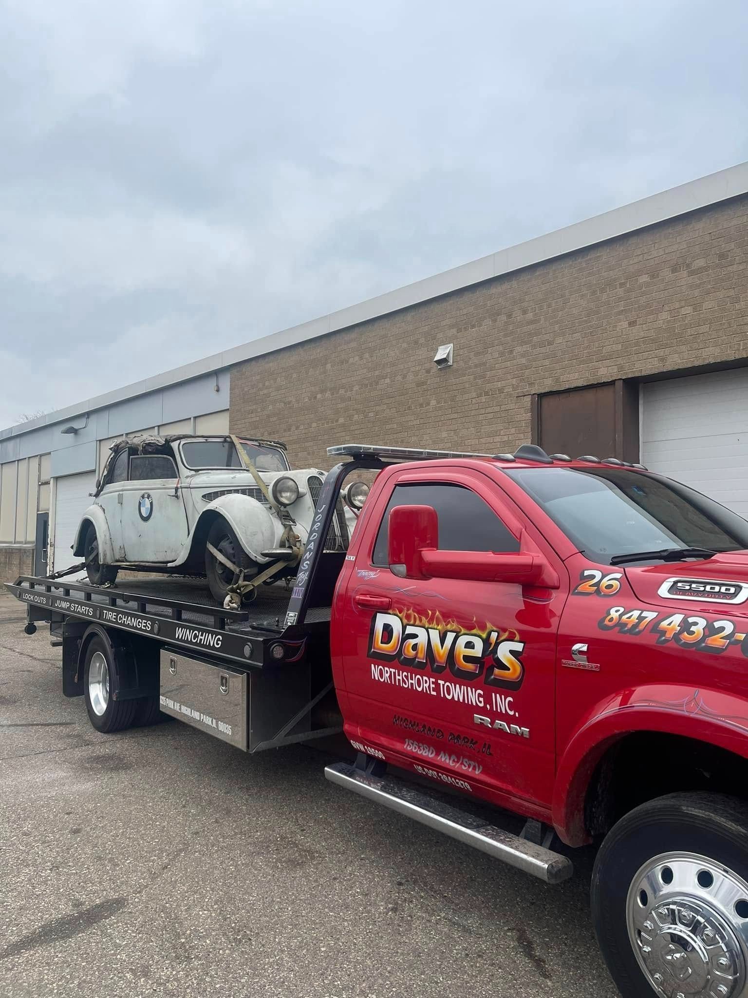 A red tow truck is towing a white car.