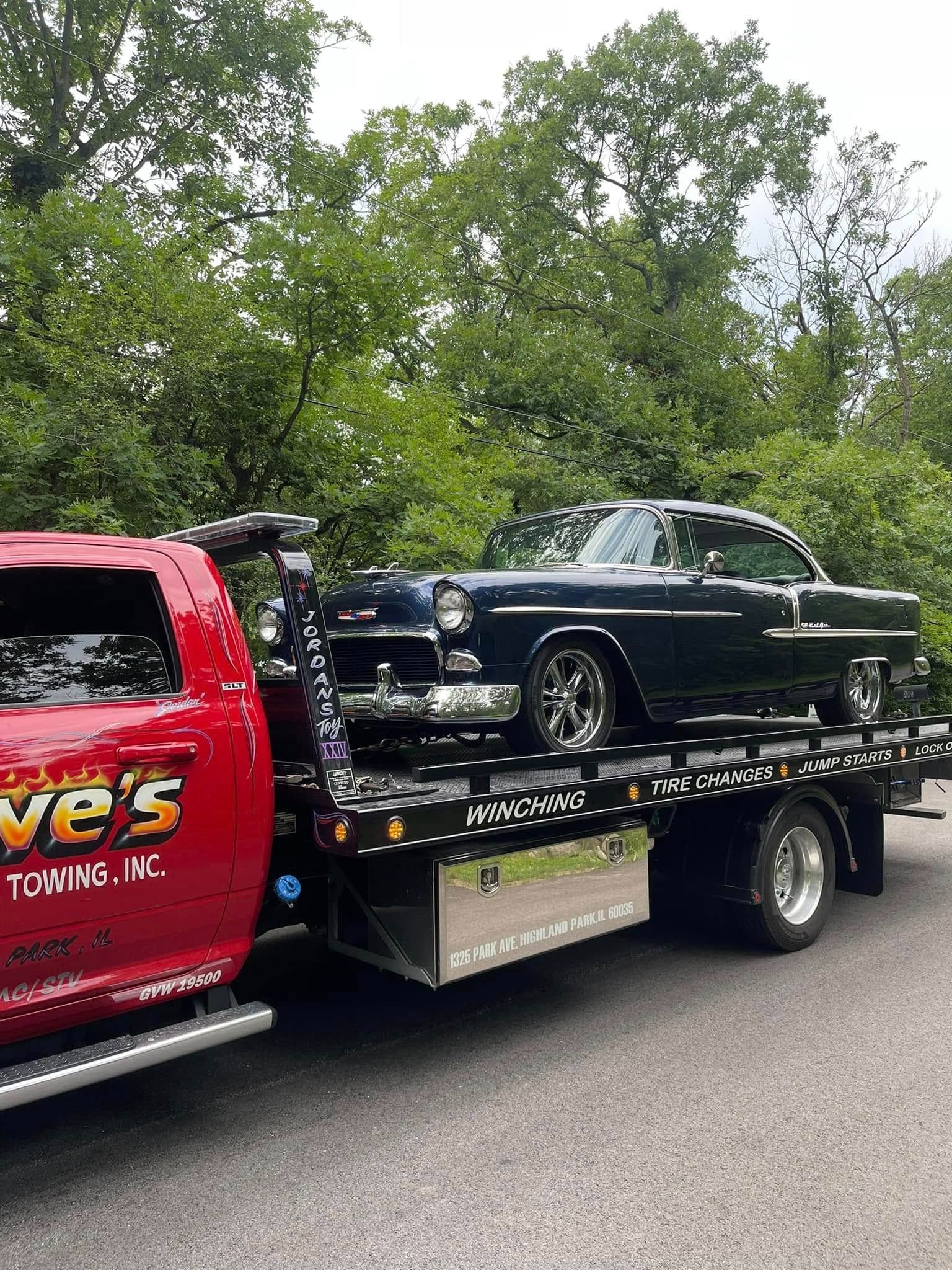 A black car is being towed by a tow truck.
