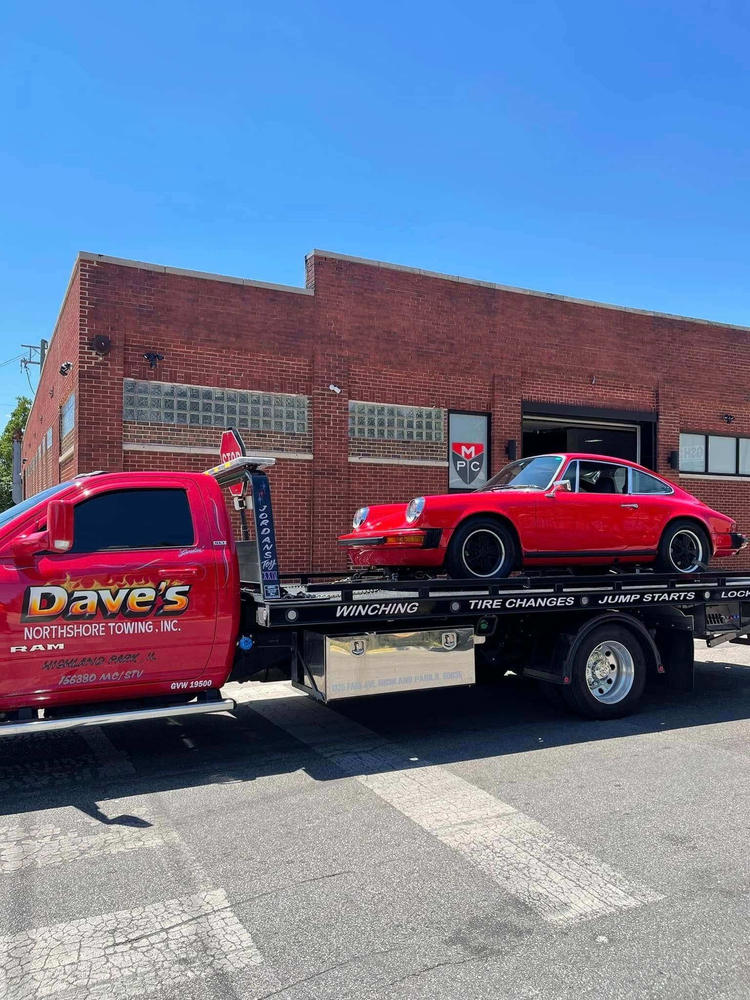 A red car is being towed by a tow truck.