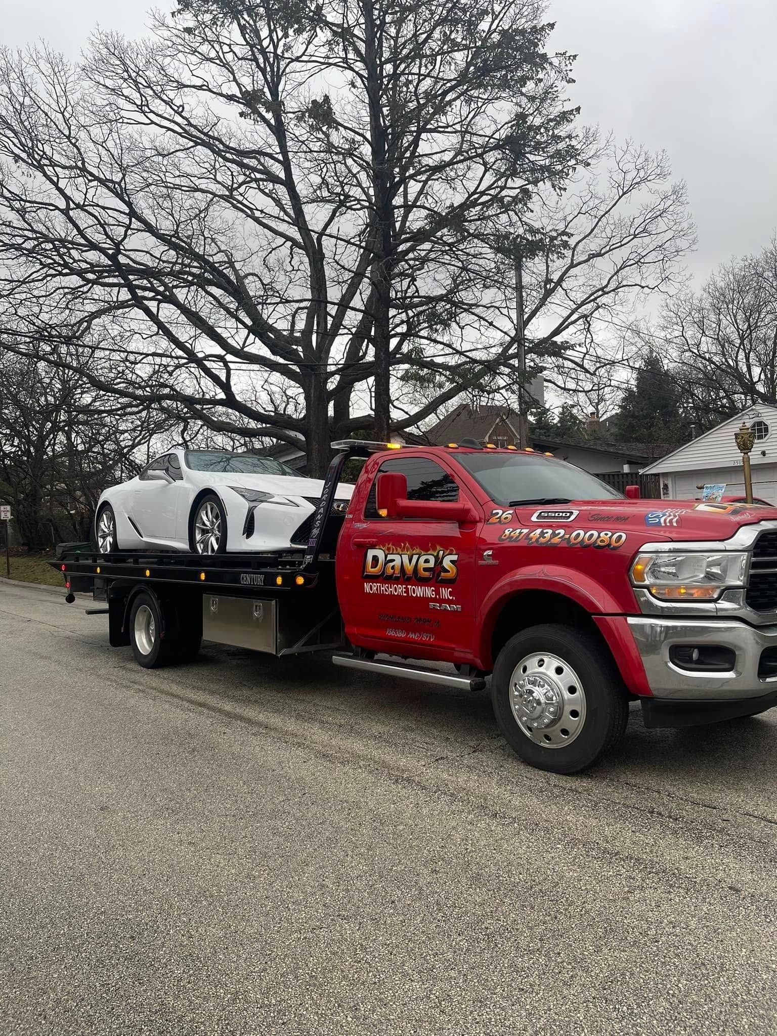 A red tow truck is towing a white sports car.
