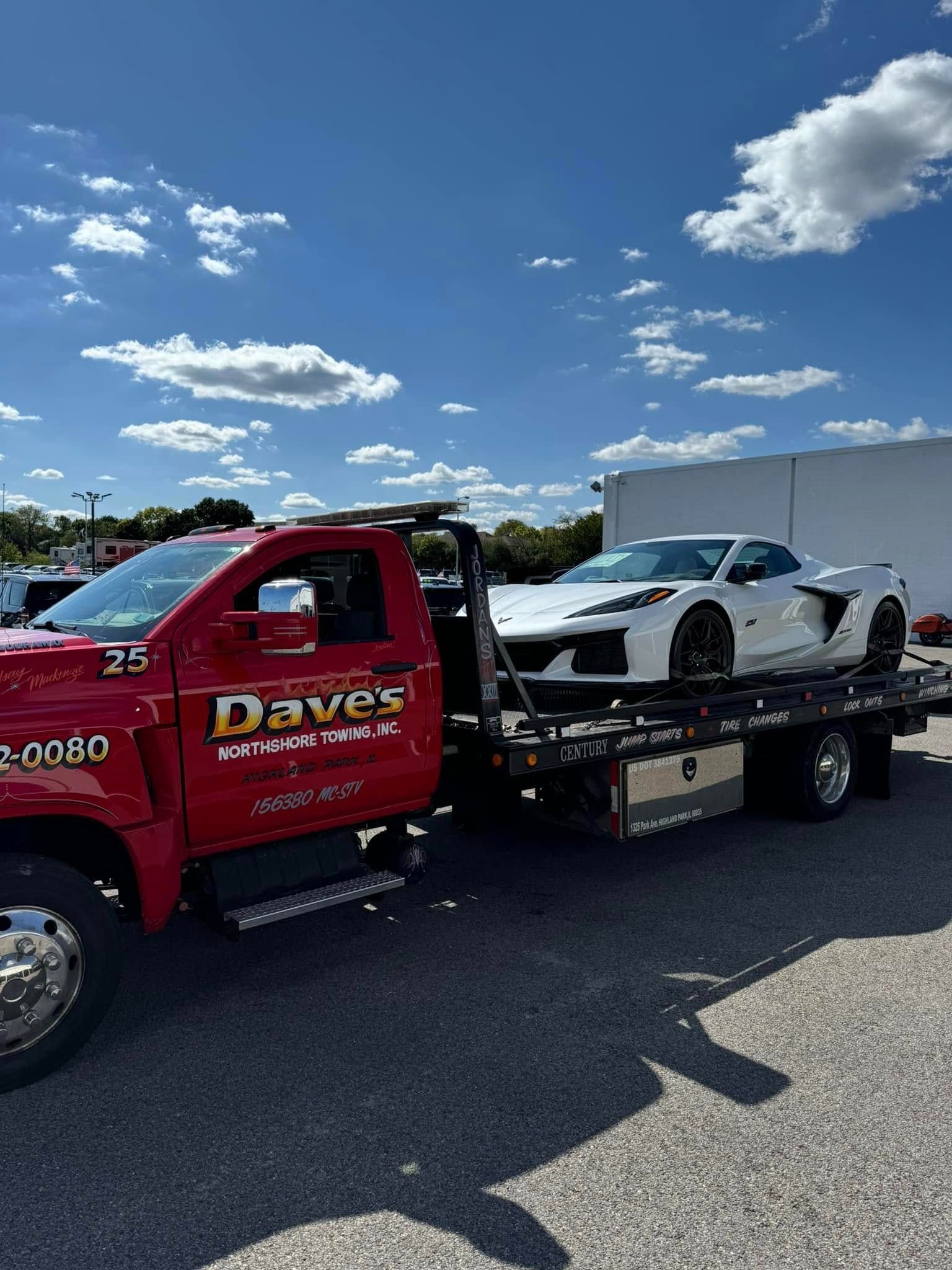 A red tow truck is towing a white sports car.