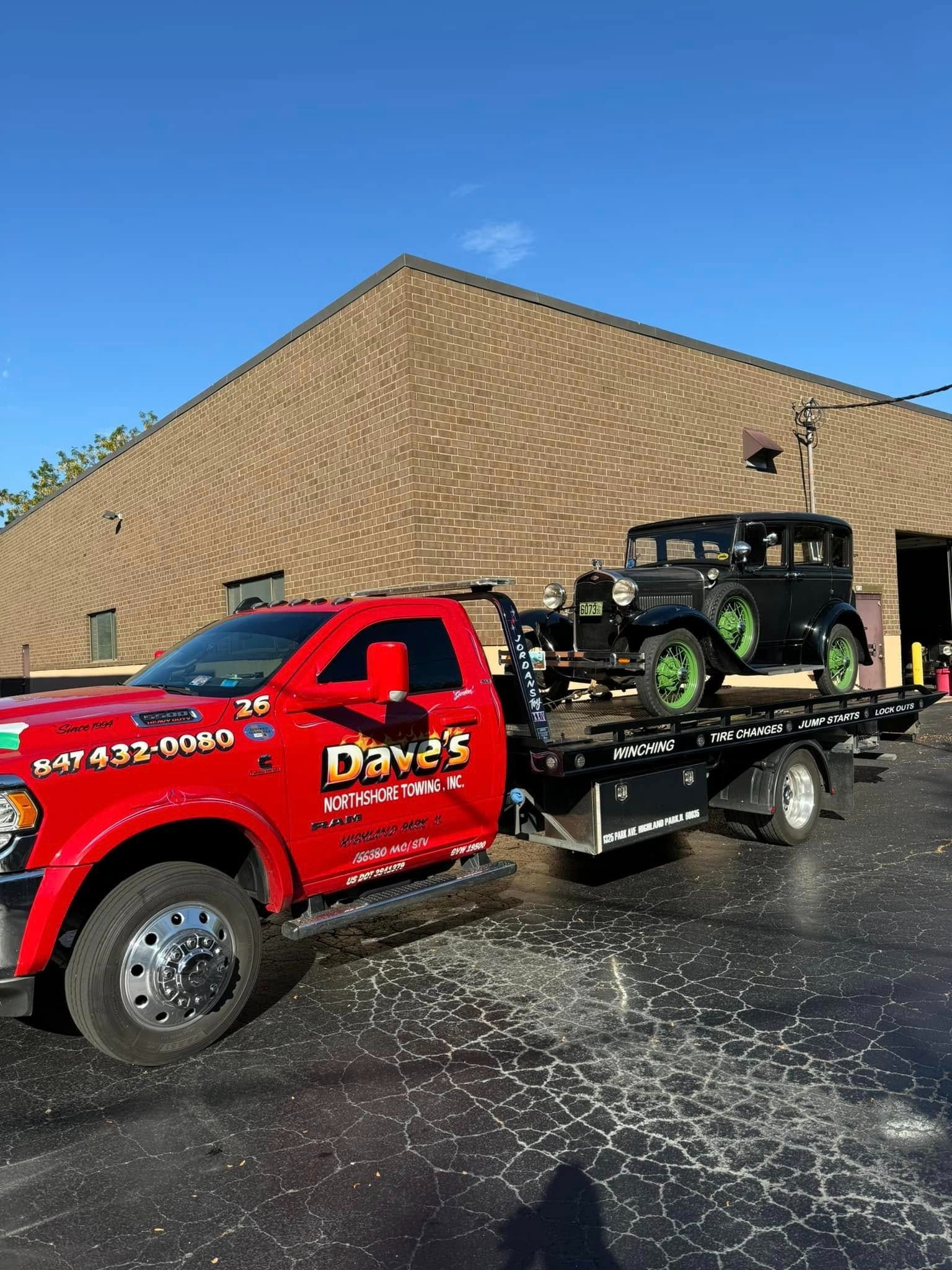 A red tow truck is towing a black car in front of a building.