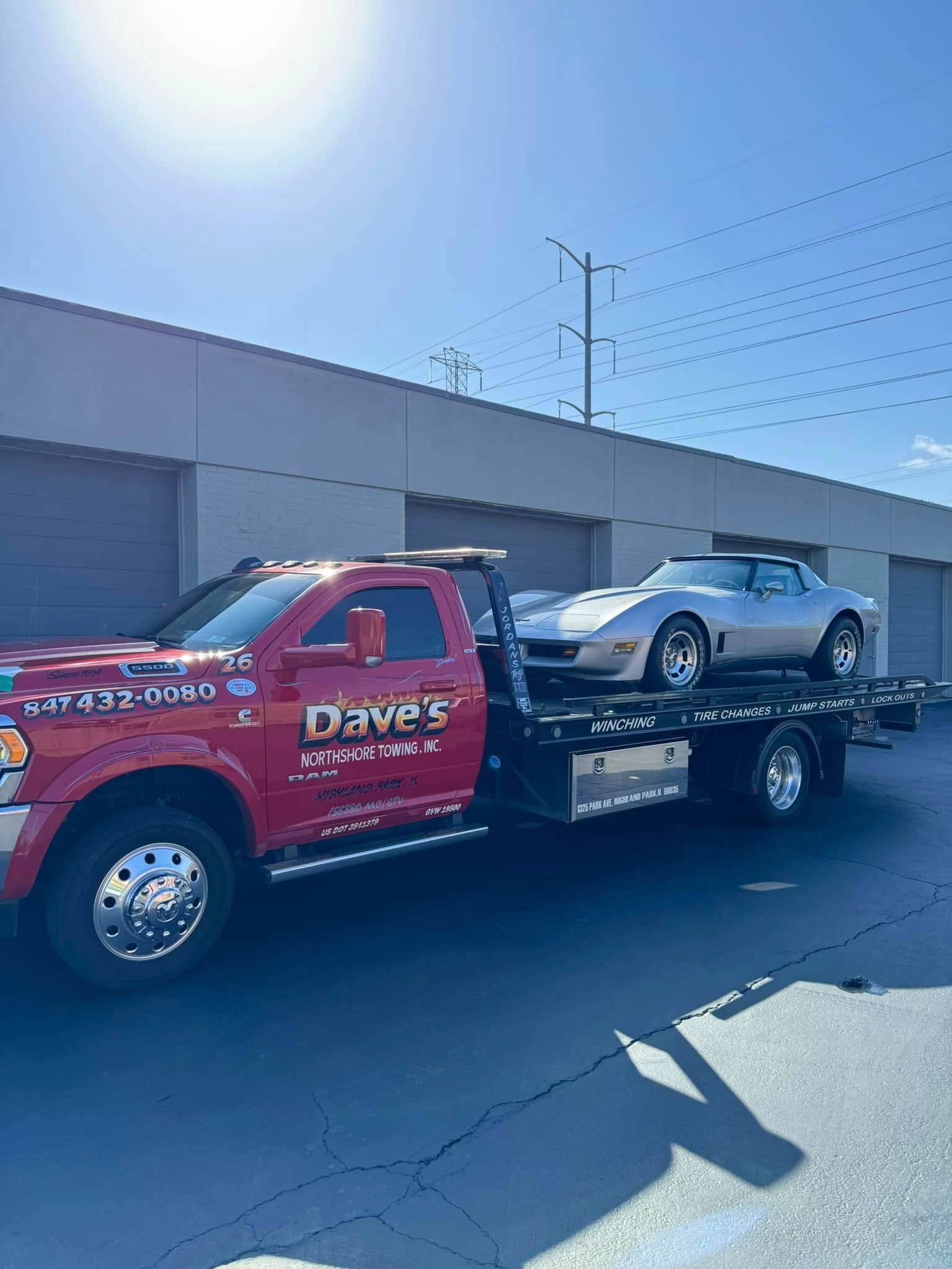 A tow truck is carrying a corvette on the back of it.