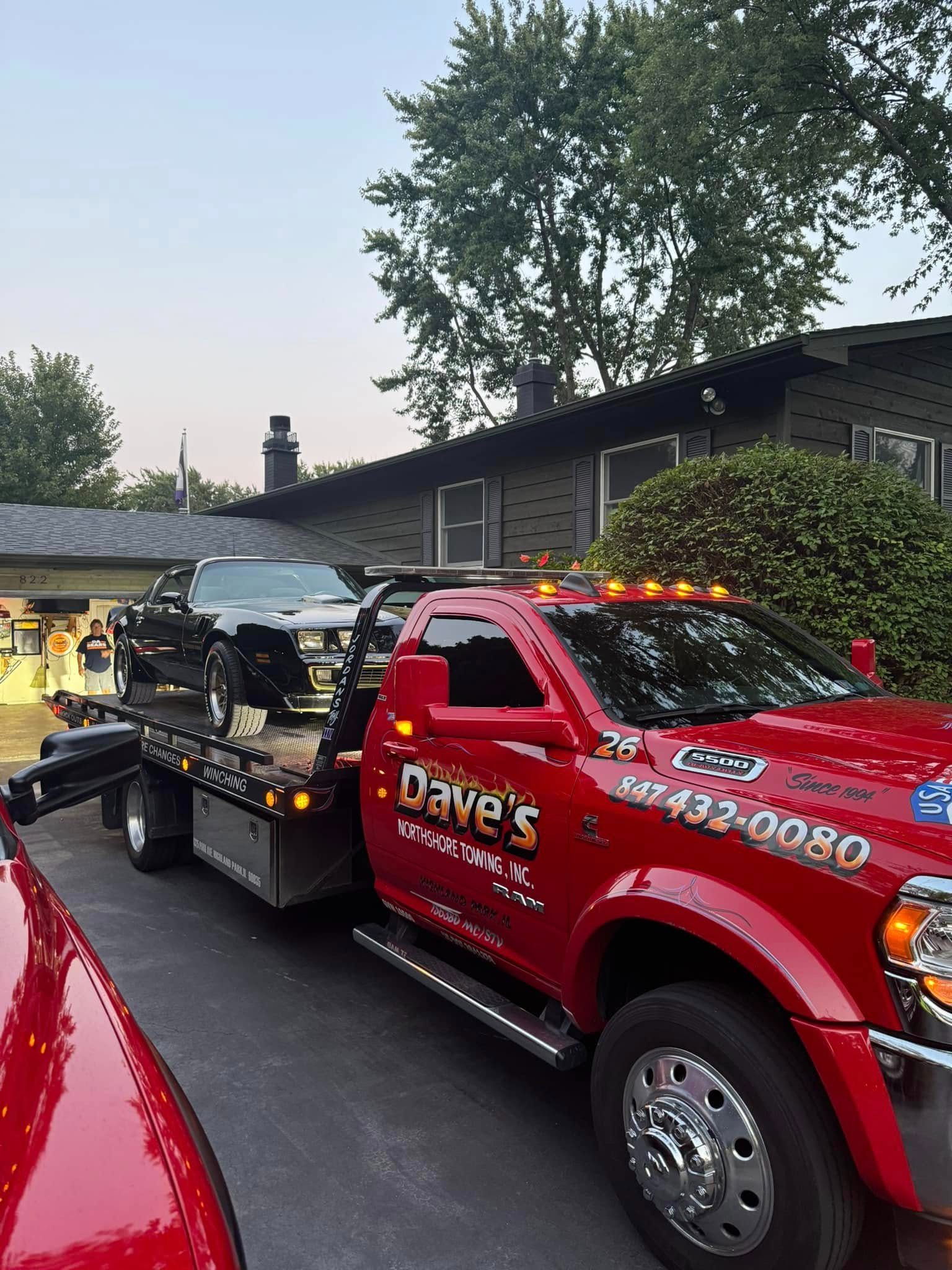 A red tow truck is towing a car in front of a house.