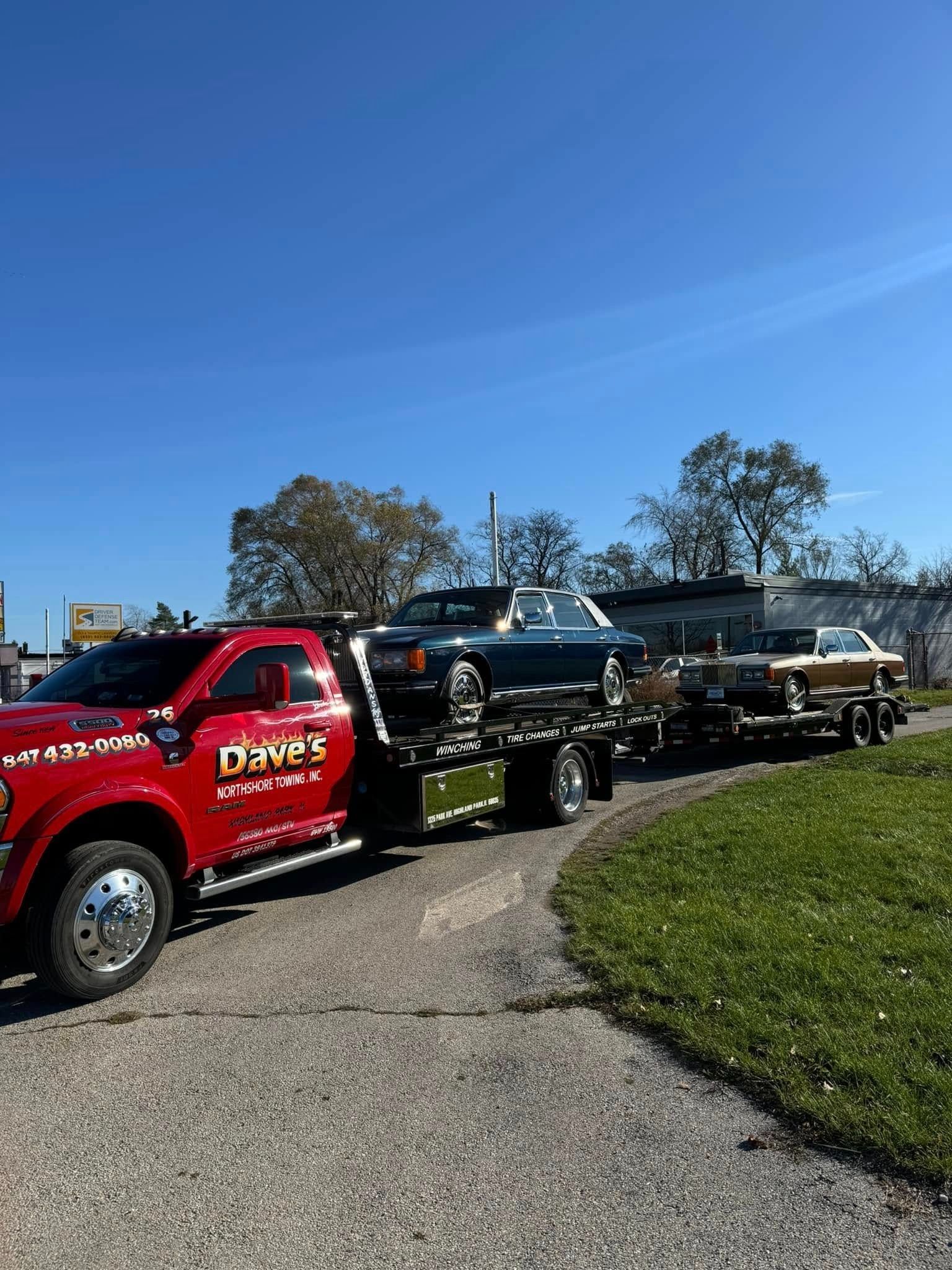 A red tow truck is towing two cars down a road.