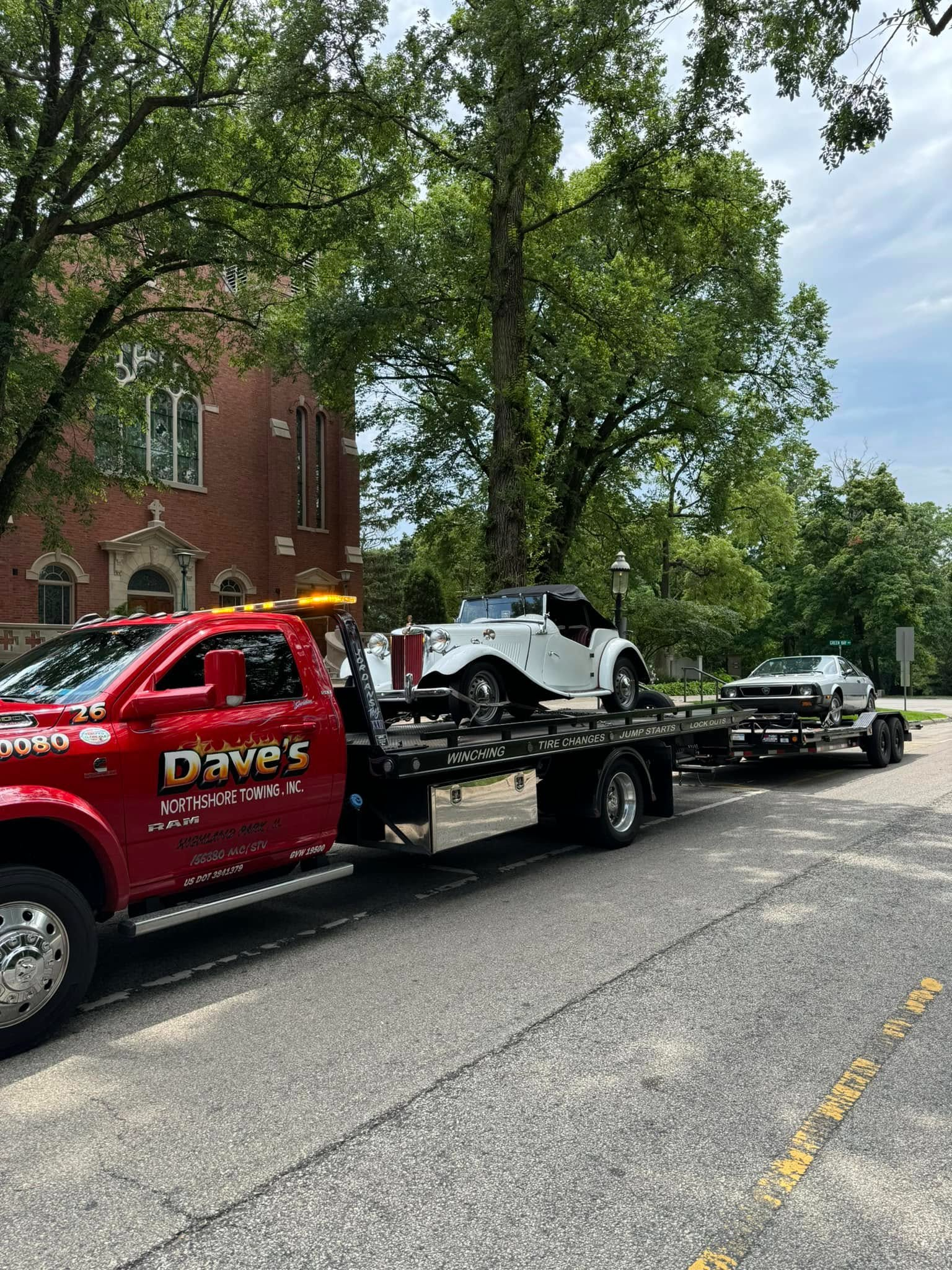 A red tow truck is towing a white car down a street.
