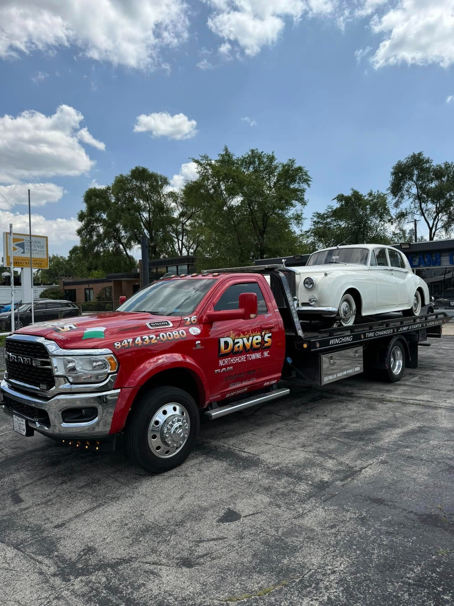 A red tow truck is towing a white car in a parking lot.