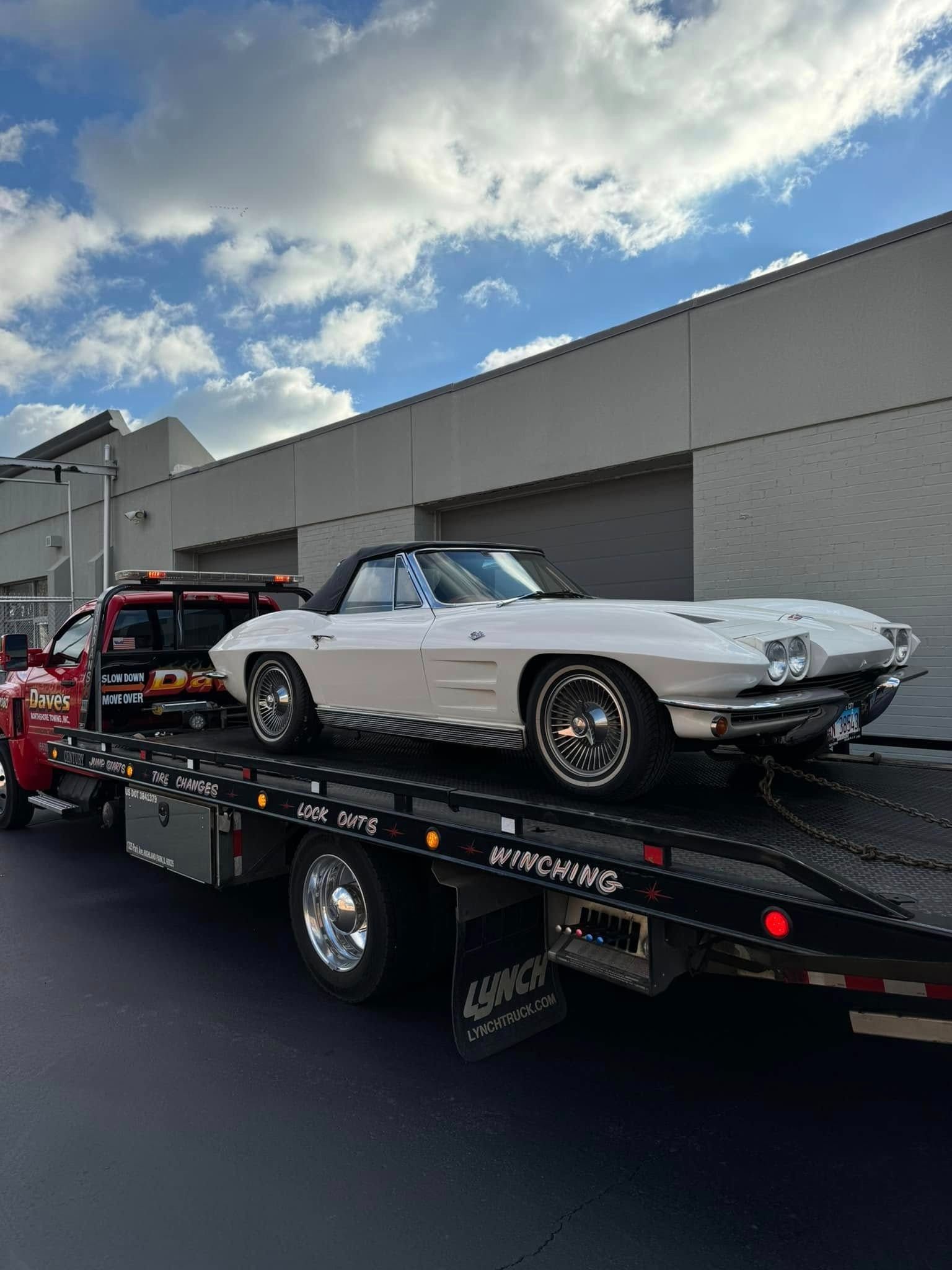 A white corvette is being towed by a tow truck.