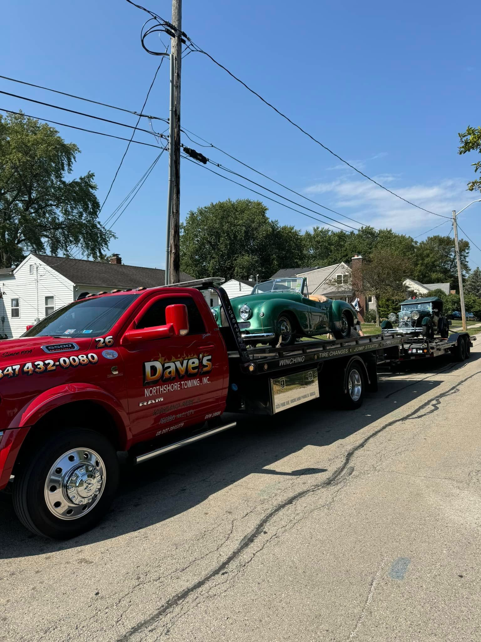 A red tow truck is towing a green car down a street.