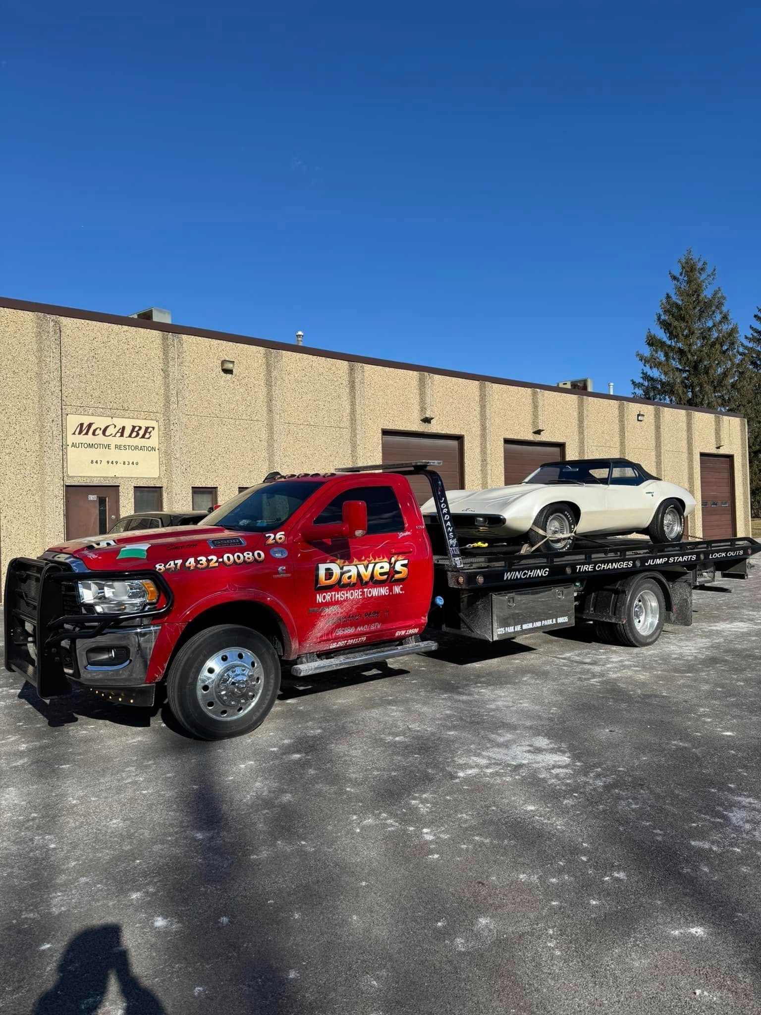 A red tow truck is towing a white car in front of a building.