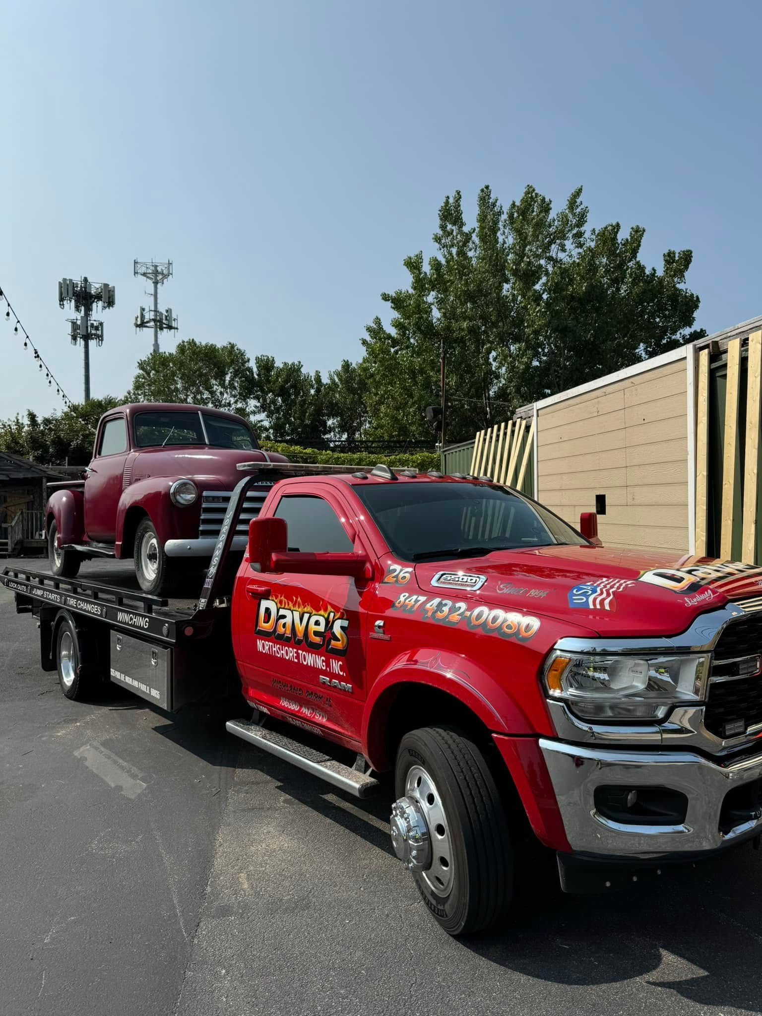 A red tow truck with a red truck on the back is parked on the side of the road.
