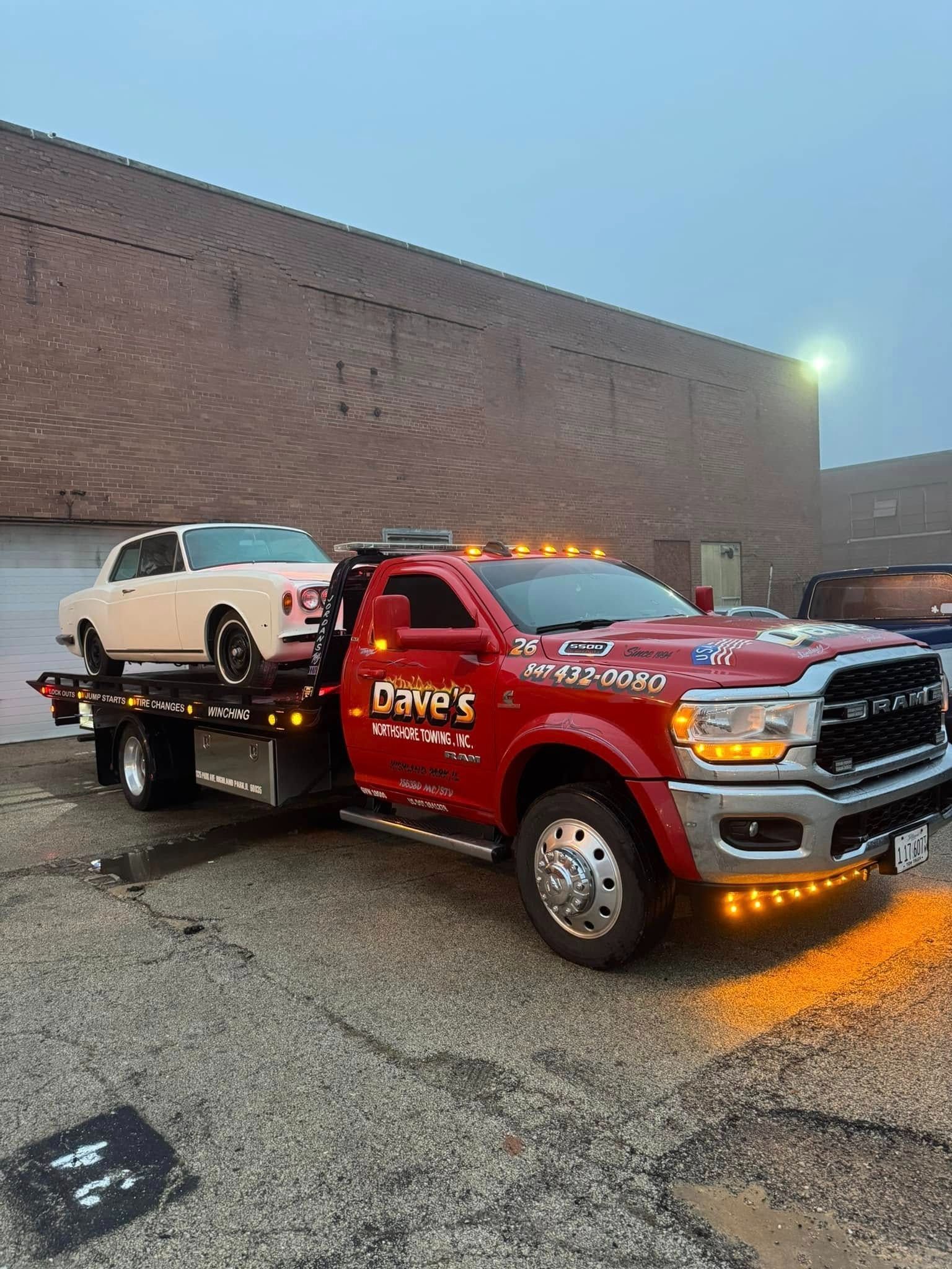 A red tow truck is towing a white car.