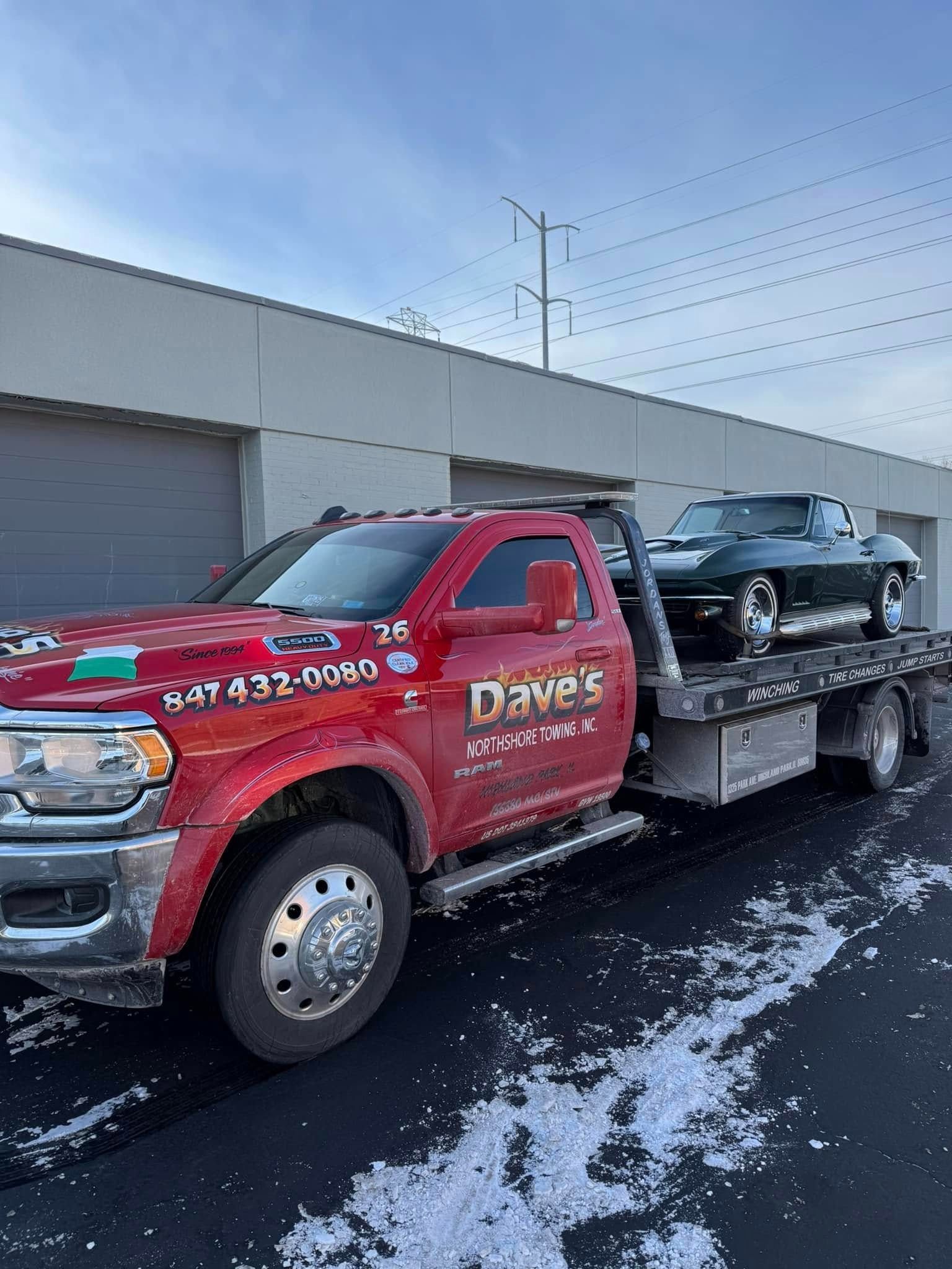 A red tow truck is towing a car in a parking lot.