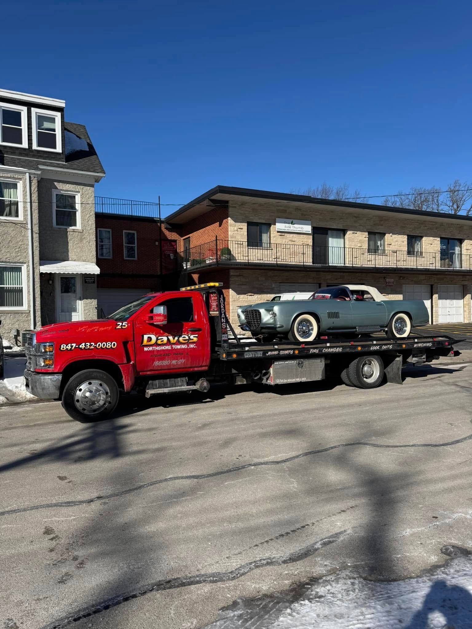 A tow truck is towing a car in front of a house.