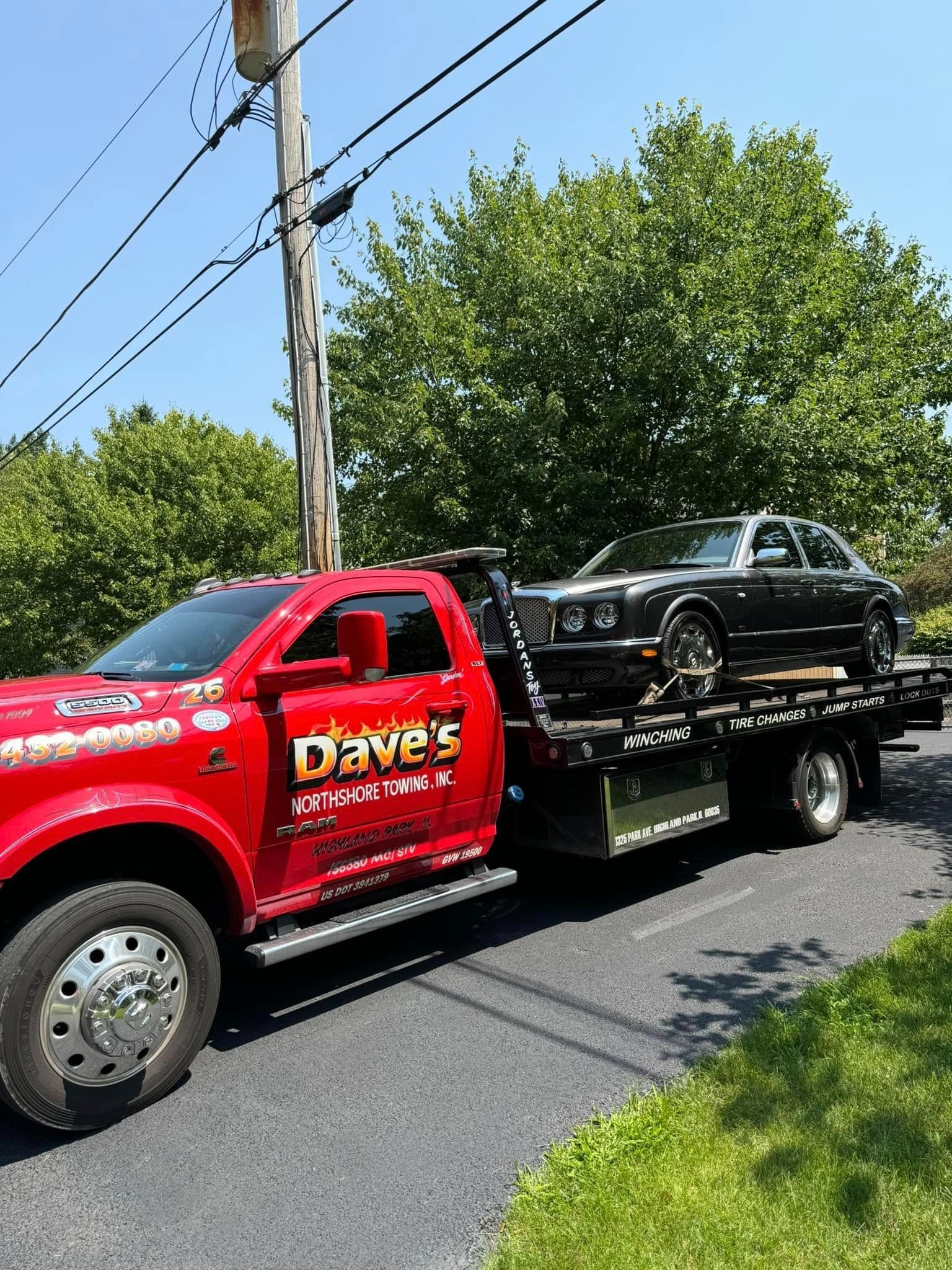 A red tow truck is towing a black car down a road.