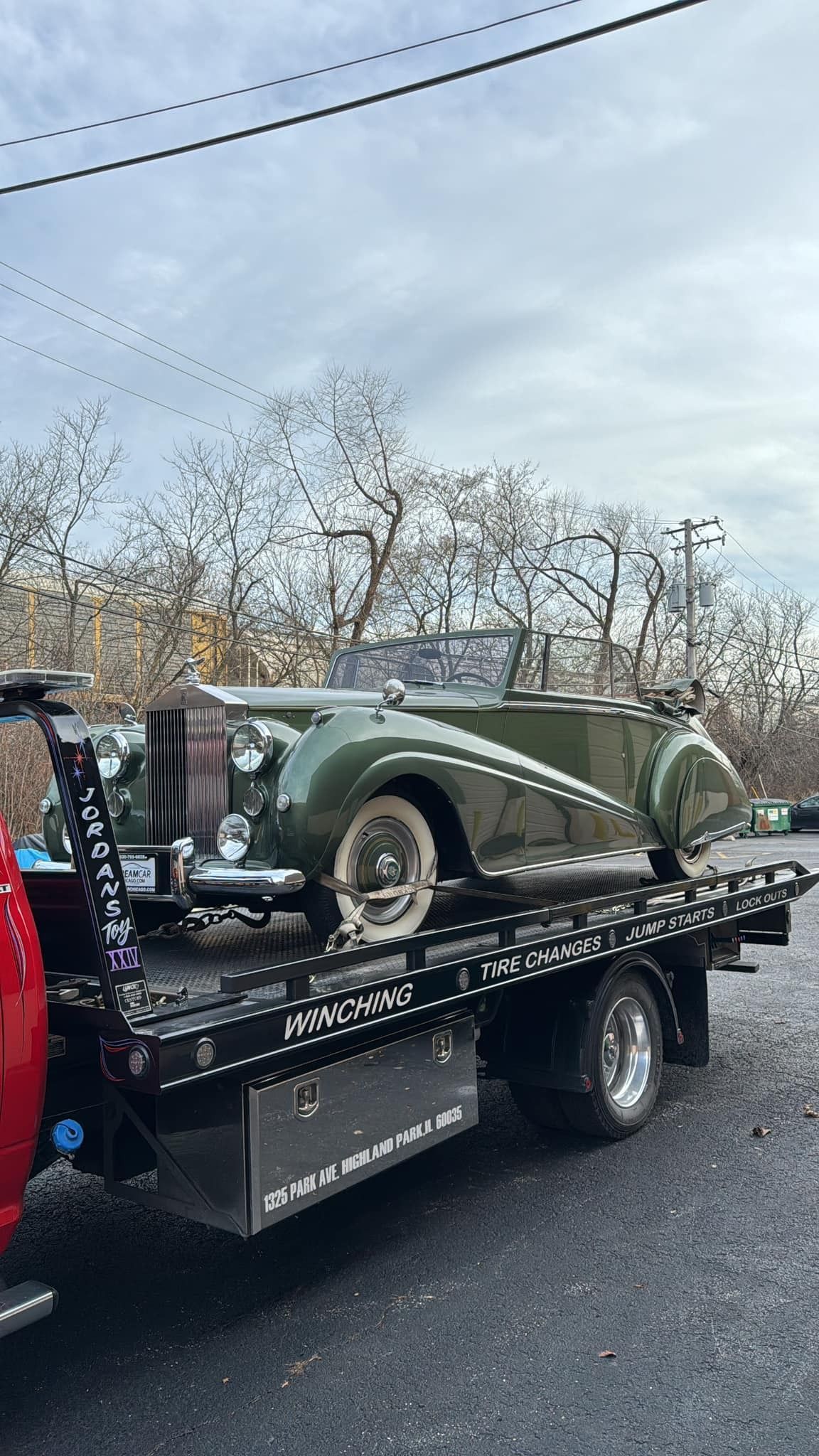 A green car is being towed by a tow truck.