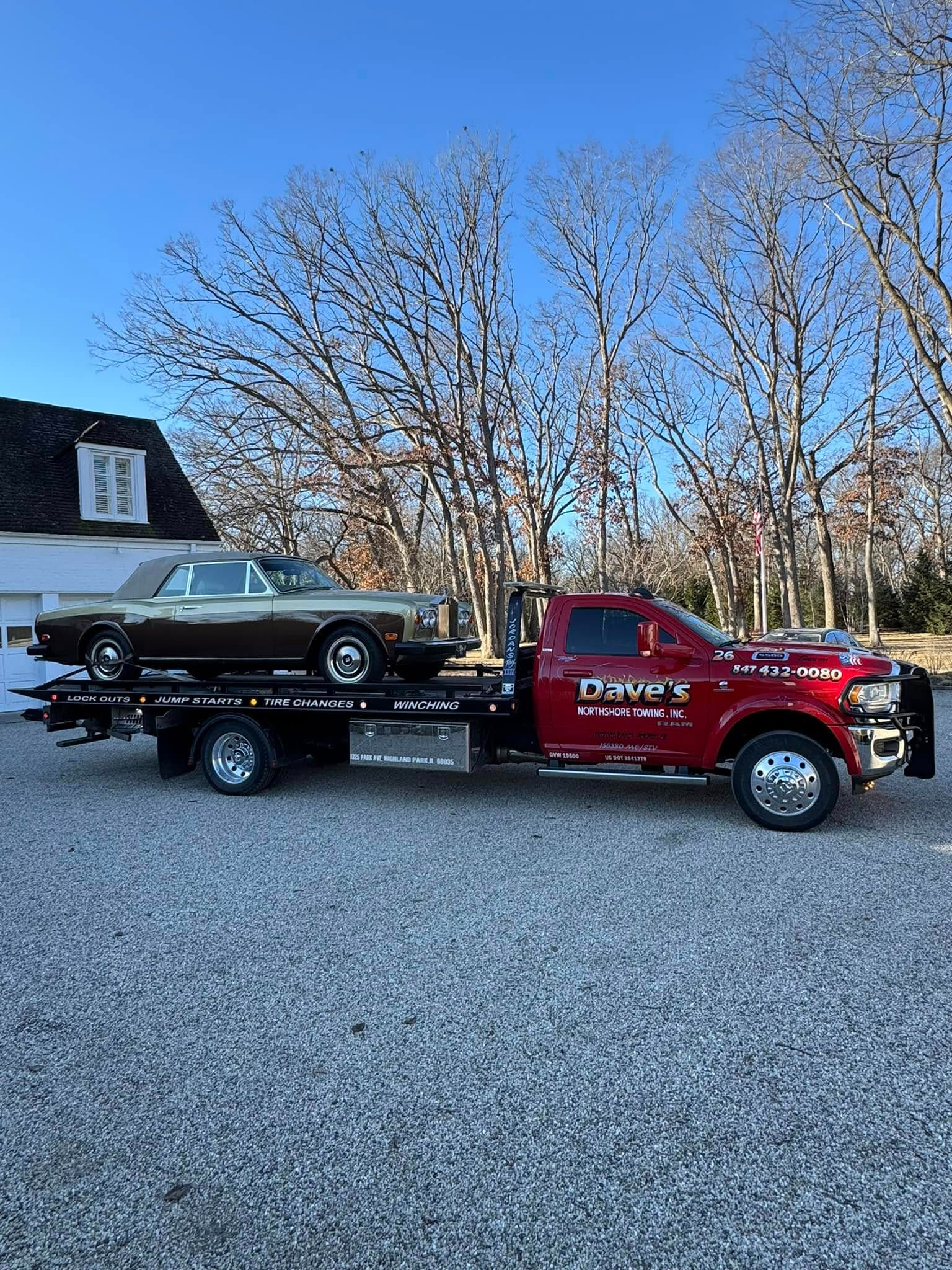 A tow truck is towing a car in a gravel lot.