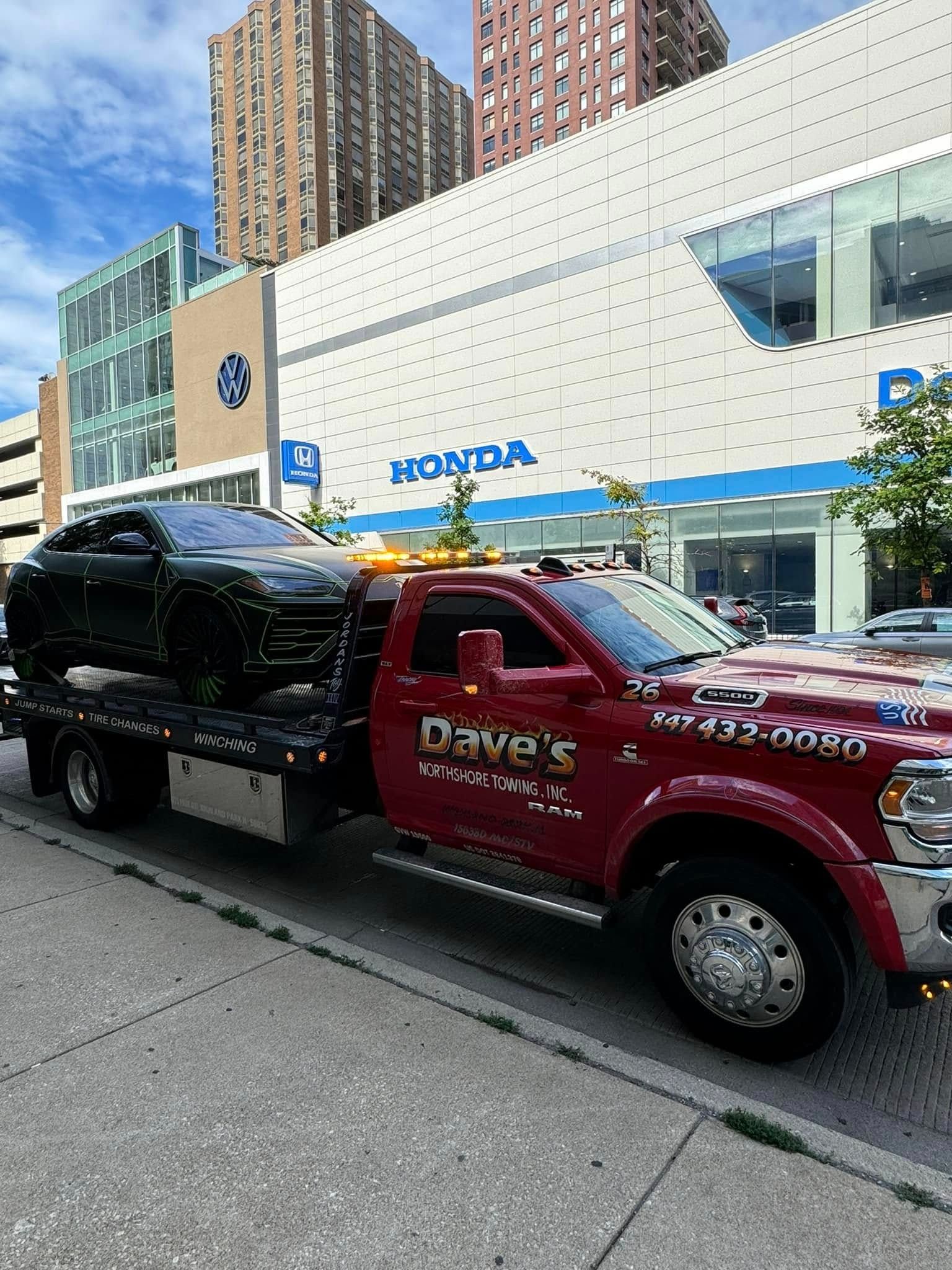 A red tow truck is towing a black suv on a city street.