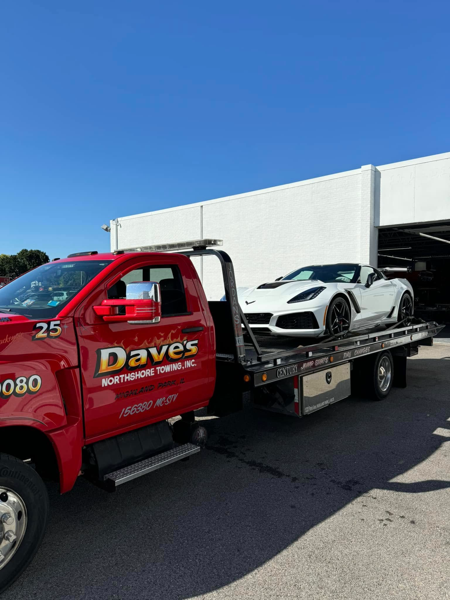 A red tow truck is towing a white sports car.