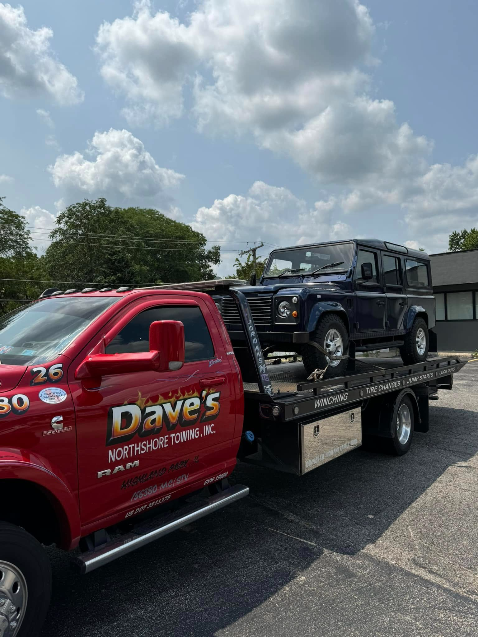 A red tow truck is towing a blue jeep.