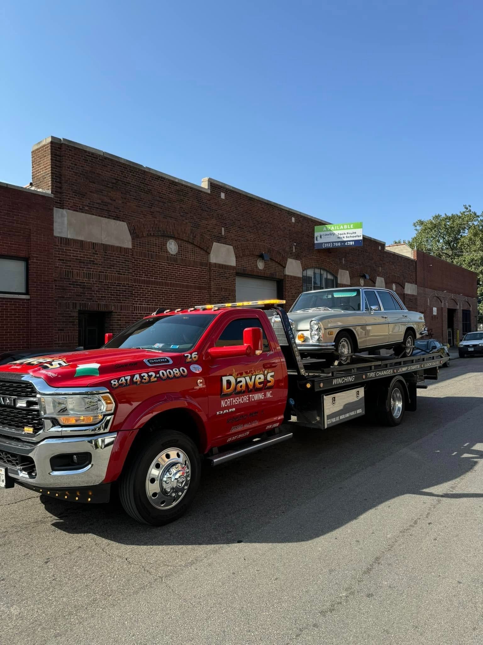 A red tow truck with two cars on the back is parked in front of a building.