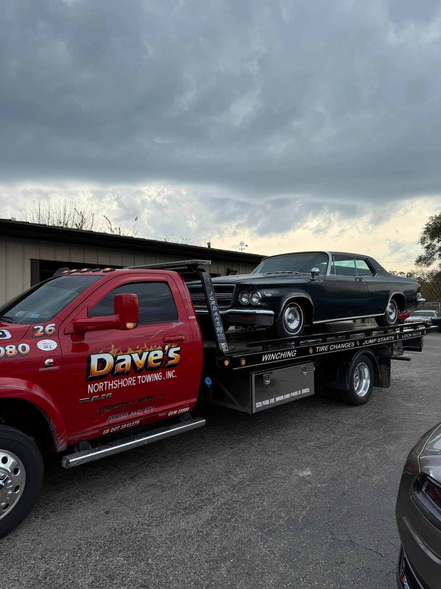 A red tow truck is towing a black car in a parking lot.