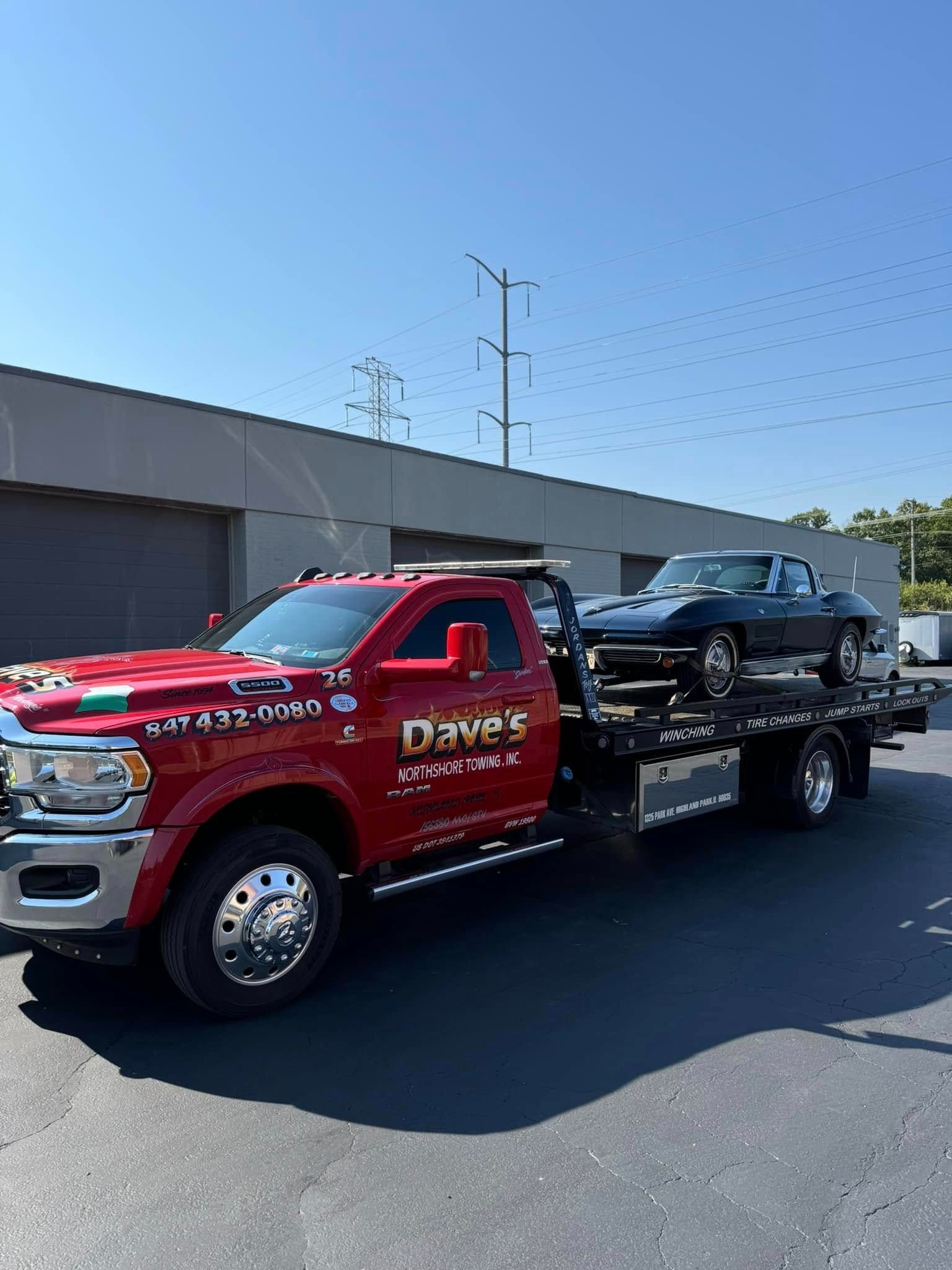 A red tow truck is towing a black car.