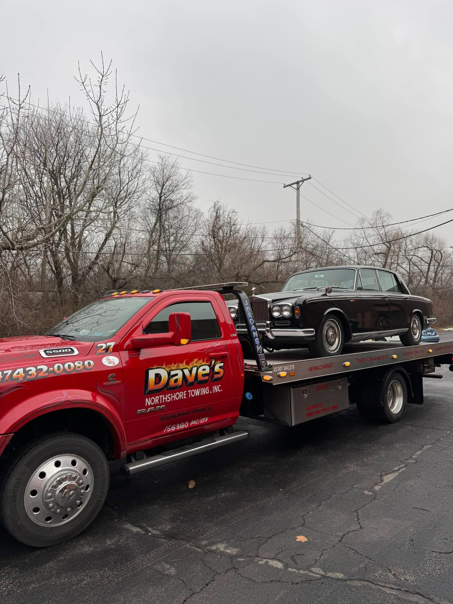 A red tow truck is towing a black car in a parking lot.
