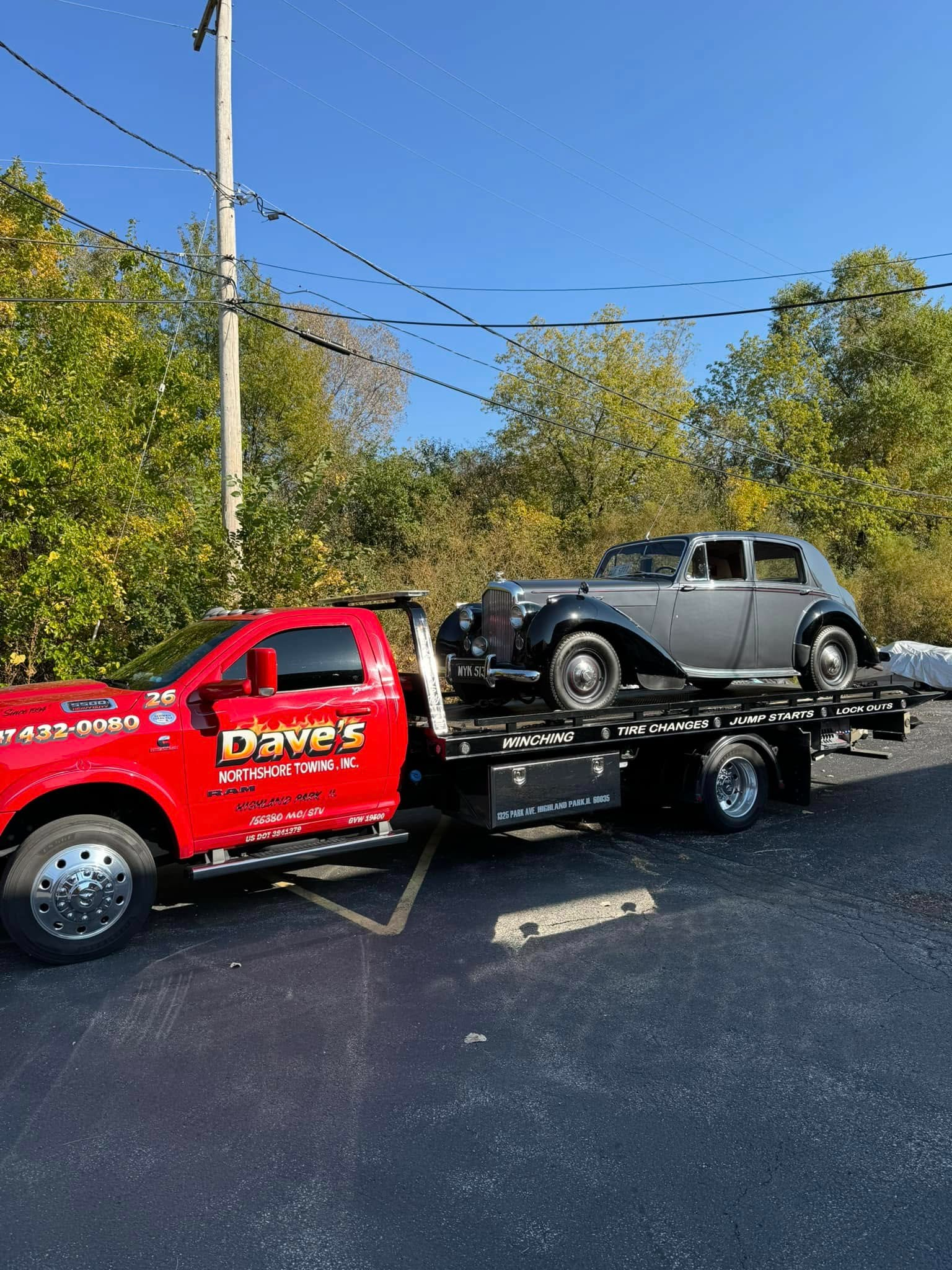 A red tow truck is towing a black car in a parking lot.